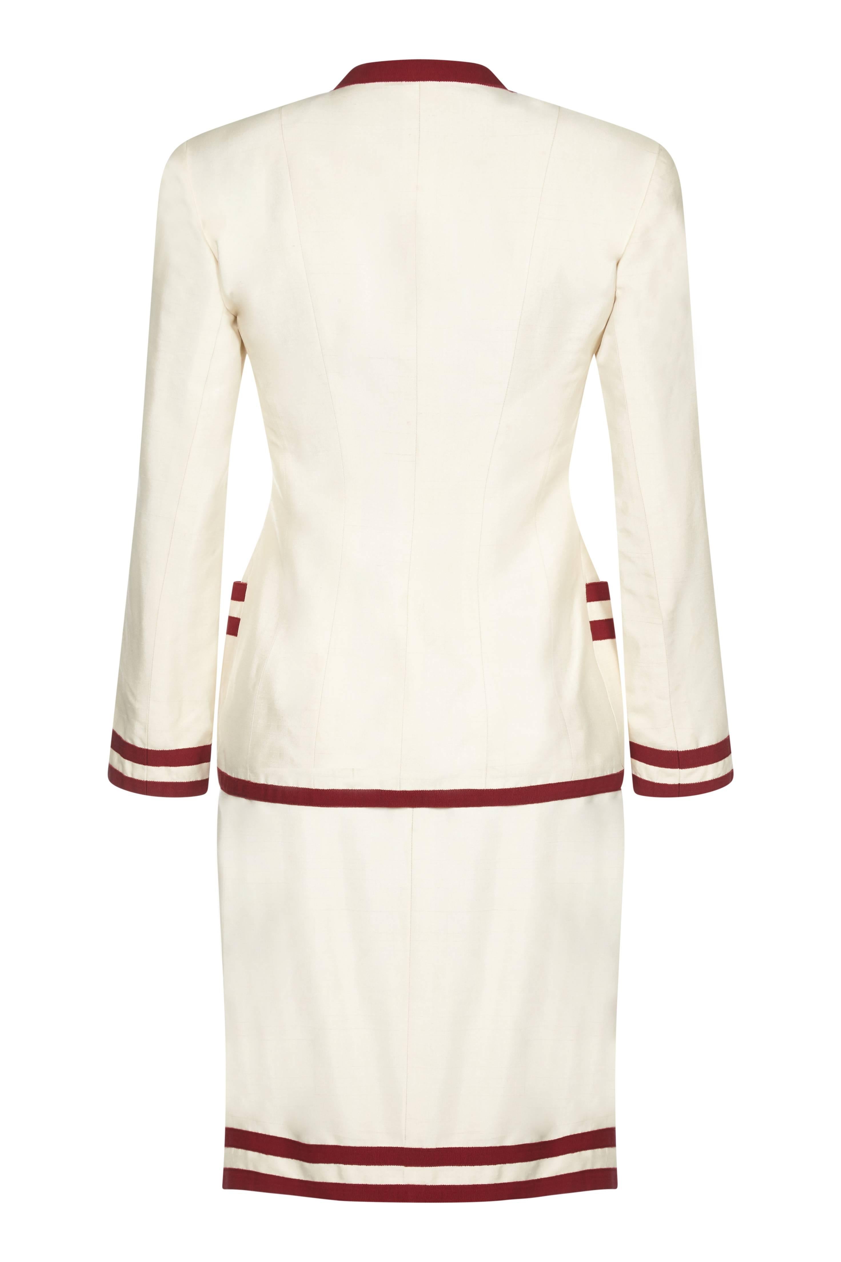 This smart early to mid 1990s Chanel cream silk 2-piece suit with grosgrain ribbon trim is in exceptional condition and perfectly exemplifies the casual chic synonymous with this classic and celebrated brand. The 100% raw silk outer of the jacket is