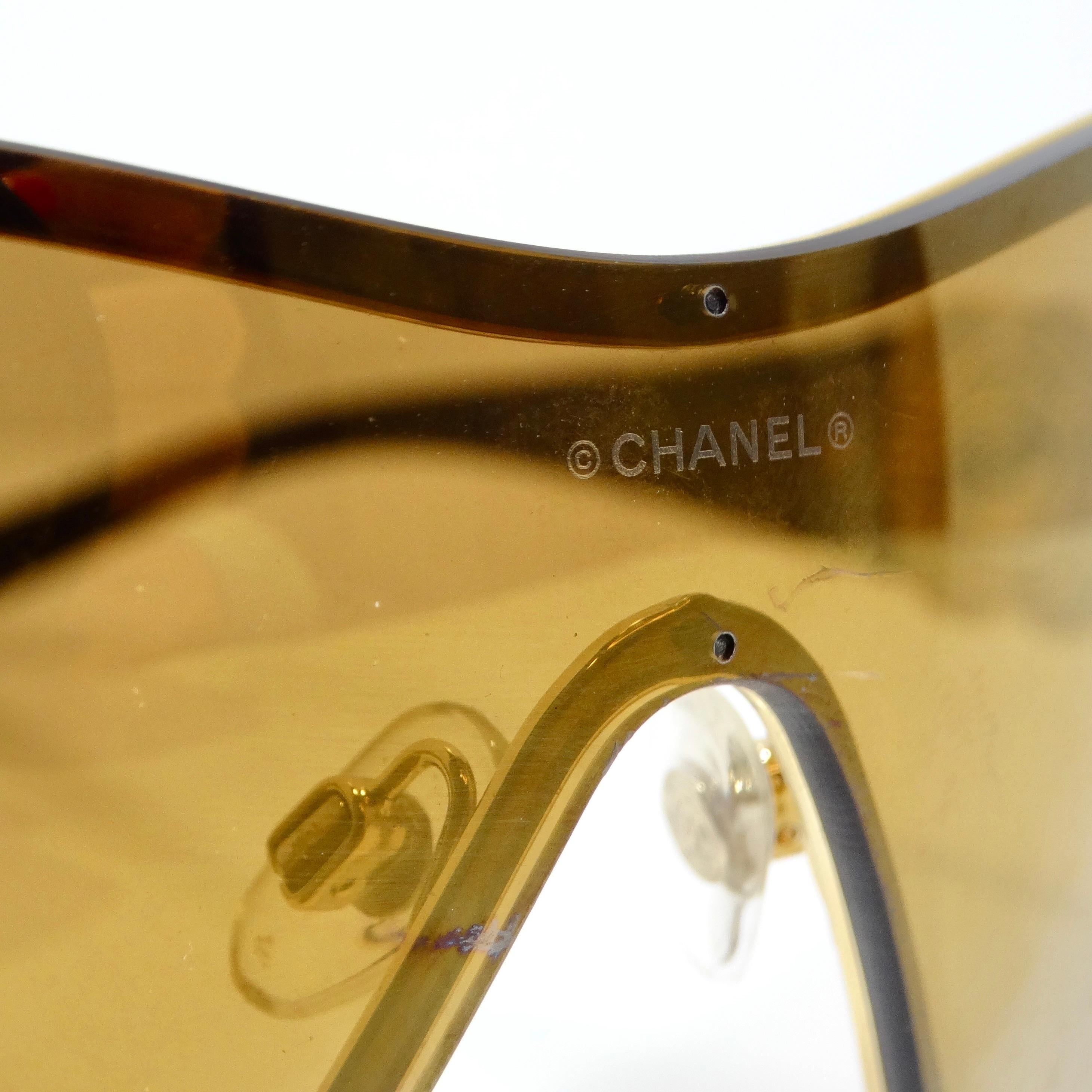 Die Chanel 1990s Gold Tone Camelia Shield Sonnenbrille ist eine bemerkenswerte Mischung aus zeitloser Eleganz und modernem Flair. Diese mit viel Liebe zum Detail gefertigte Sonnenbrille im Schildform-Stil strahlt Raffinesse und Luxus aus.

Die