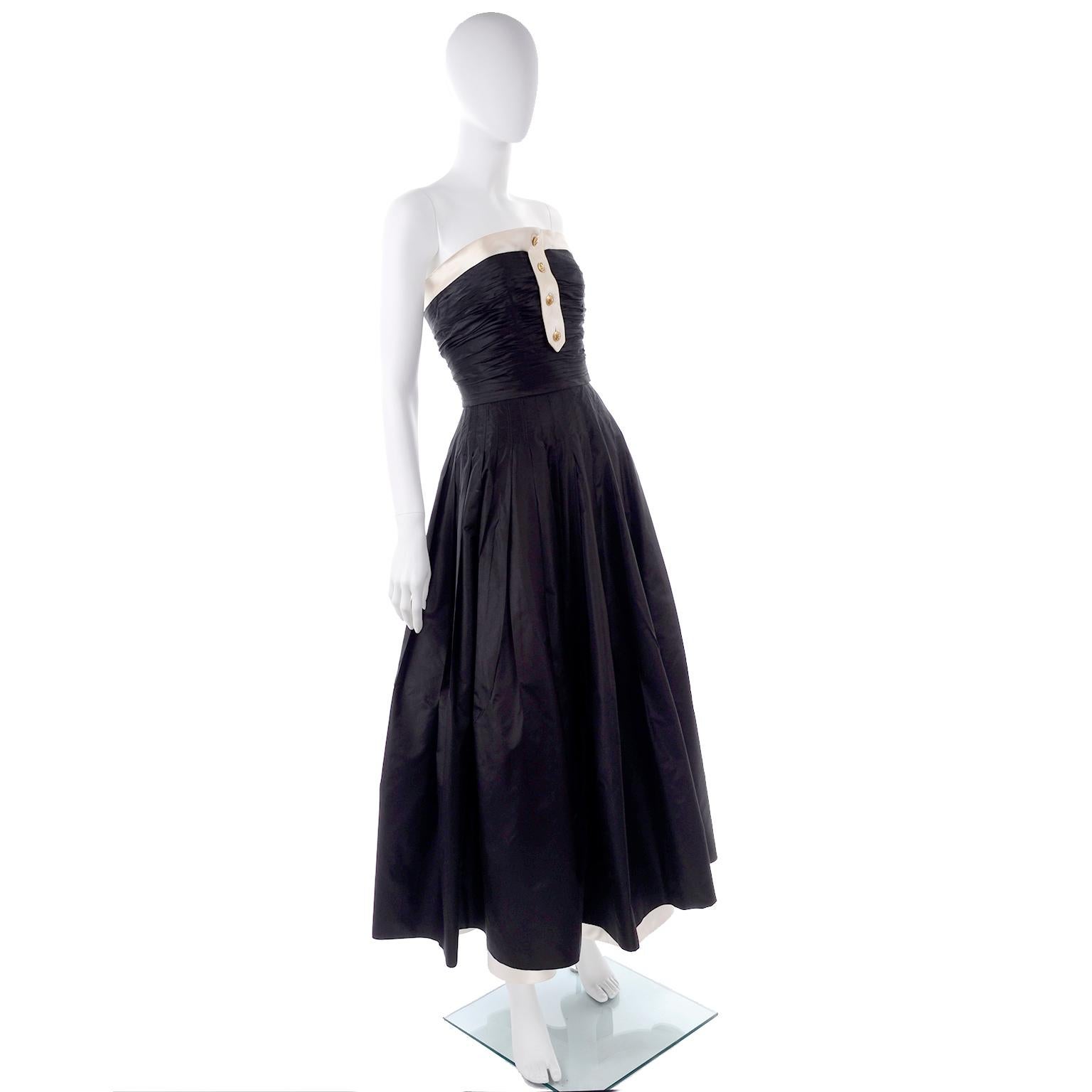 This is a beautiful Chanel 1990's Black and ivory full length dress that pays tribute to the tuxedo. This strapless evening dress is in a black silk taffeta with ivory silk trim and it has gold monogram cc buttons down the front. We particularly