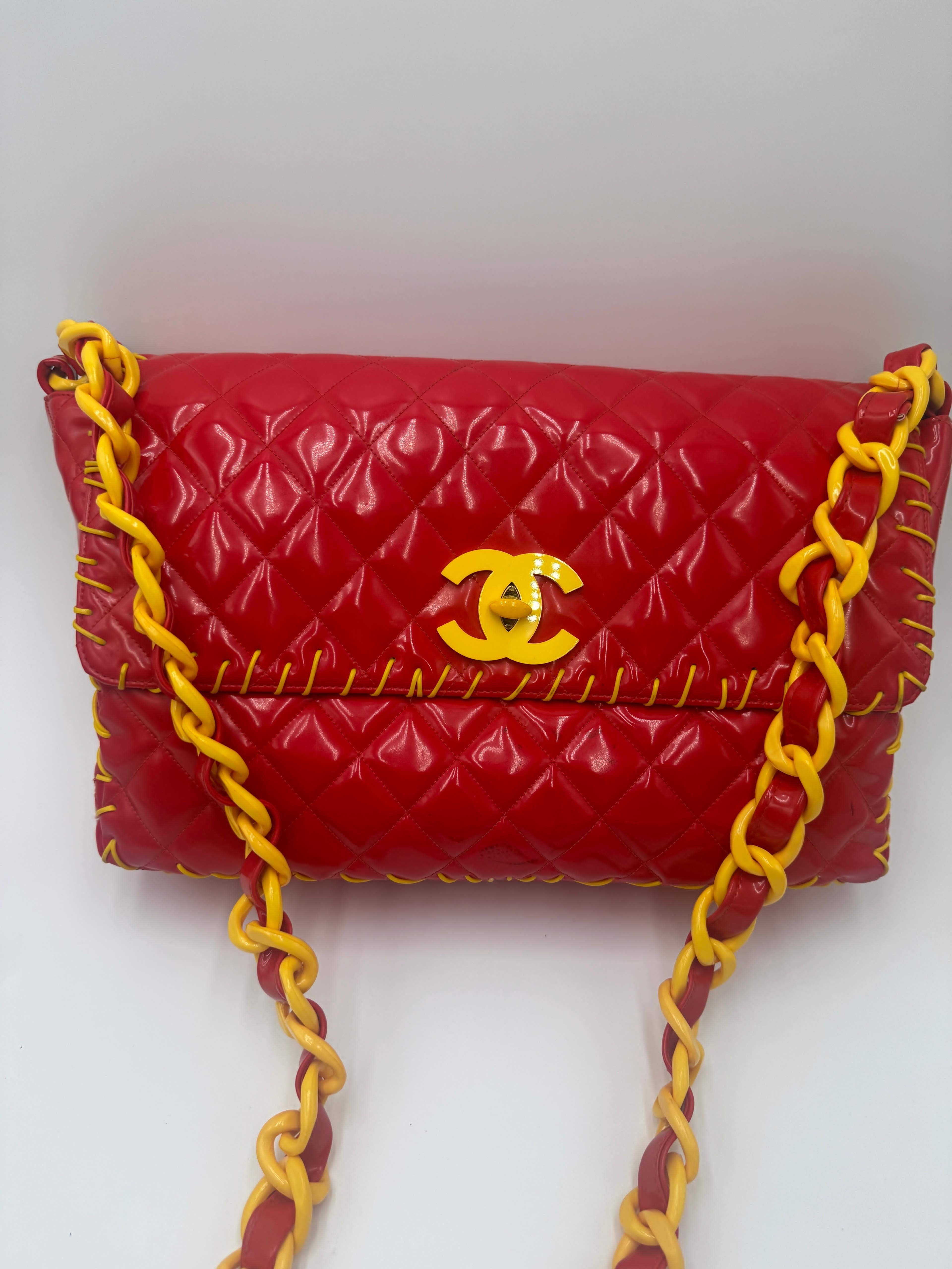 This rare Chanel Vinyl Maxi Flap Bag from 1994 features vibrant red quilted vinyl with striking yellow leather woven through the chain strap and trim. 
It includes the signature interlocking CC logo in yellow on the front flap. 
The bag measures
