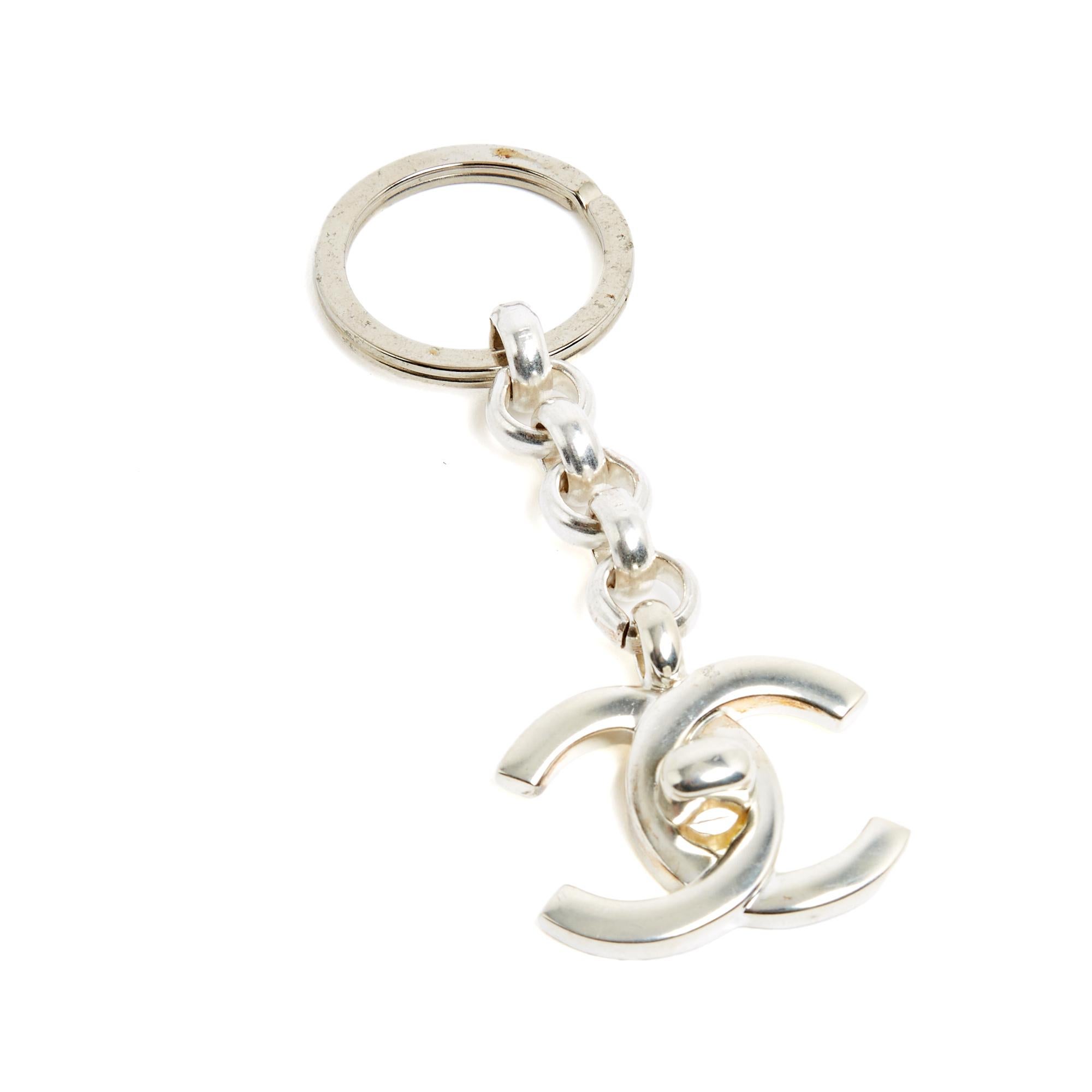 Llavero de metal plateado de la colección Chanel Primavera Verano 1996, compuesto por un gran llavero, una cadena y un gran logotipo Chanel CC (o cierre giratorio, como el cierre del bolso Timeless Classique). Longitud total del llavero 10,2 cm,