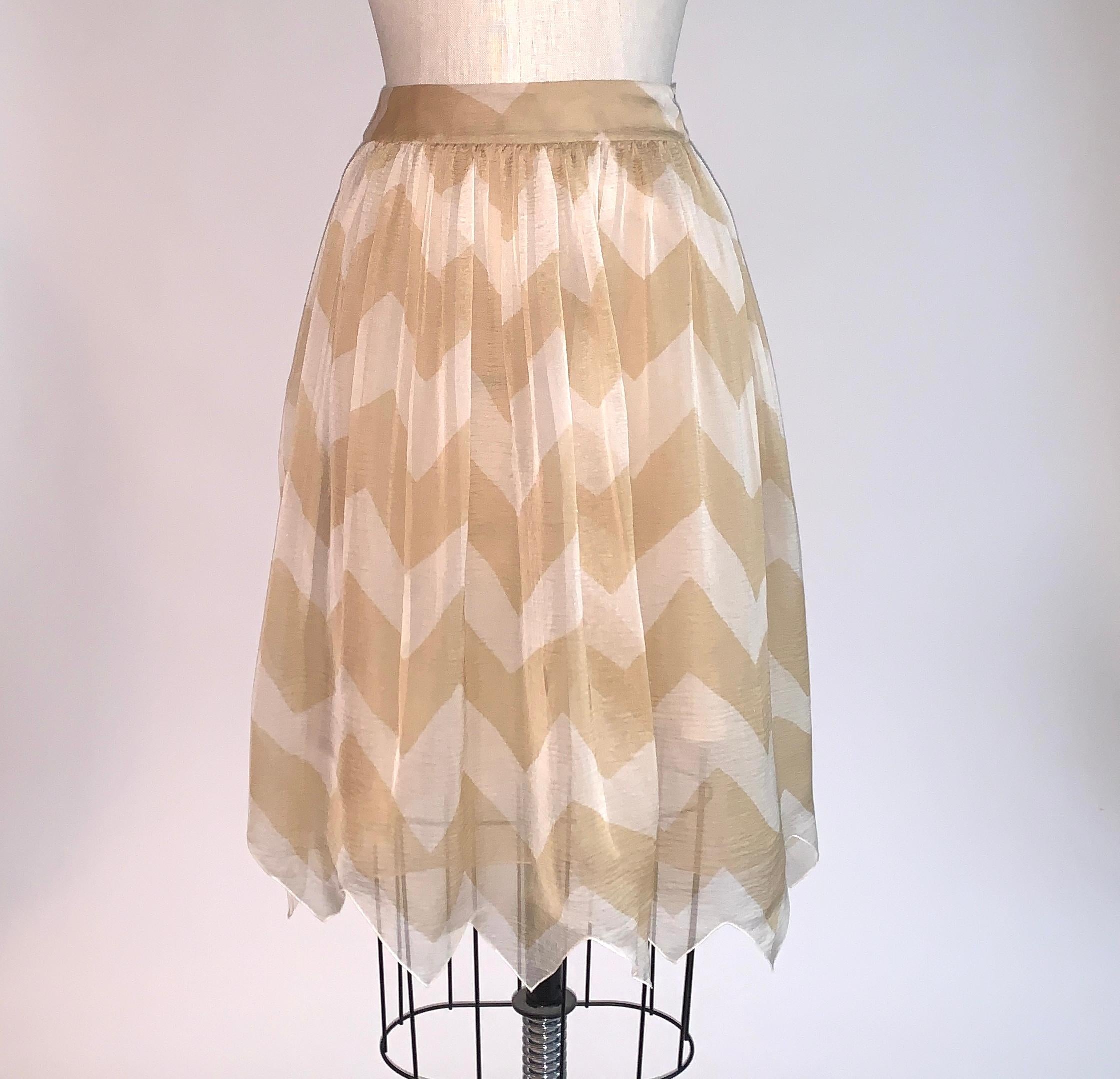 Chanel tan and white chiffon skirt in a chevron zigzag pattern with zig zag hem from the Autumn 2000 collection. Two grey shell buttons at side waist. Zipper at side interior layer.

100% silk.
Fully lined in 100% silk.

Made in France.

Size FR 34,