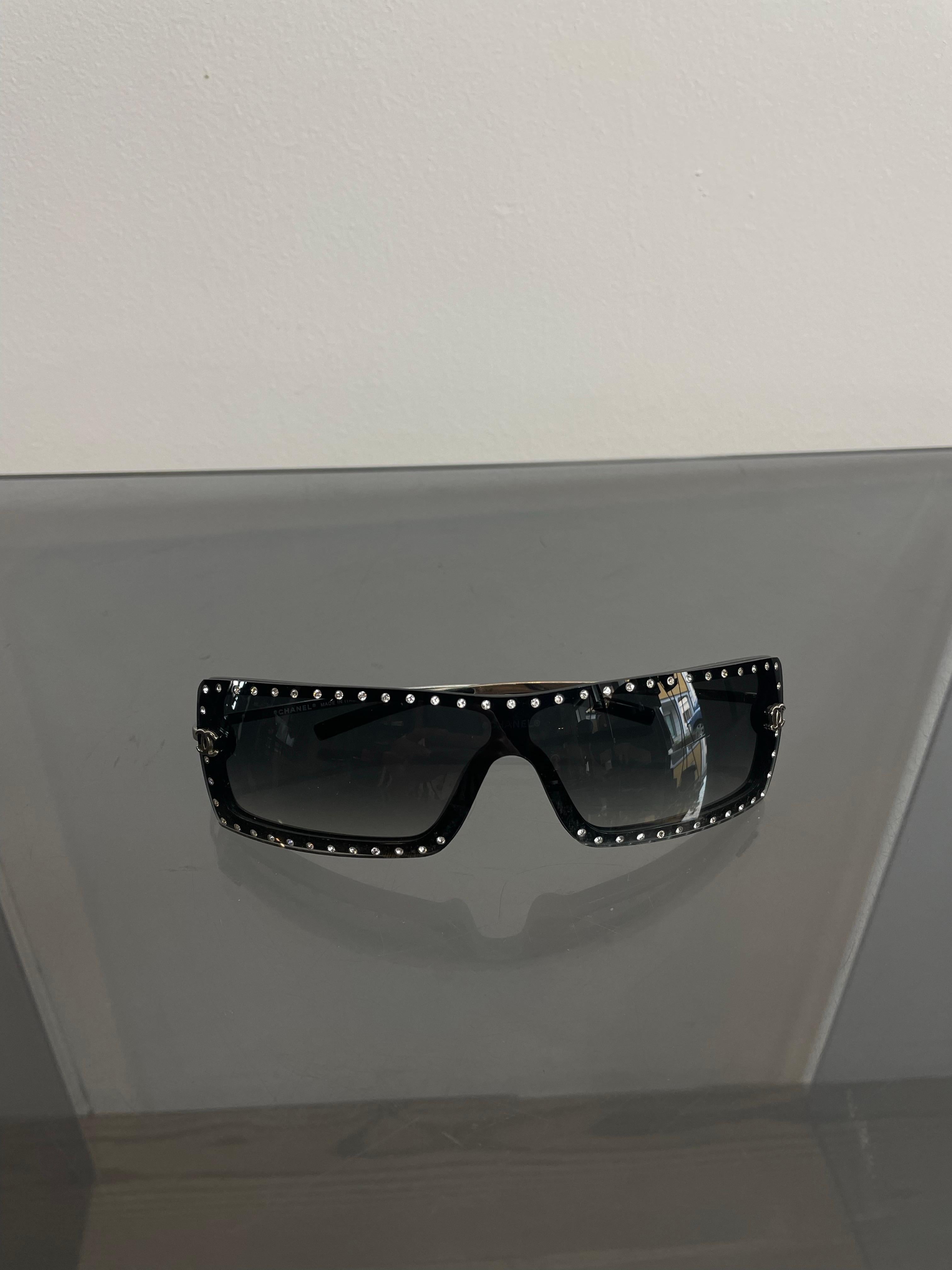 Schwarze Kunststoff-Sonnenbrille von Chanel aus den 2000er Jahren mit Strasssteinen an den Rändern. Logos und Bügel aus silbernem Metall. Sie weisen einige Gebrauchsspuren auf, sind aber im Zusammenhang gut erhalten.