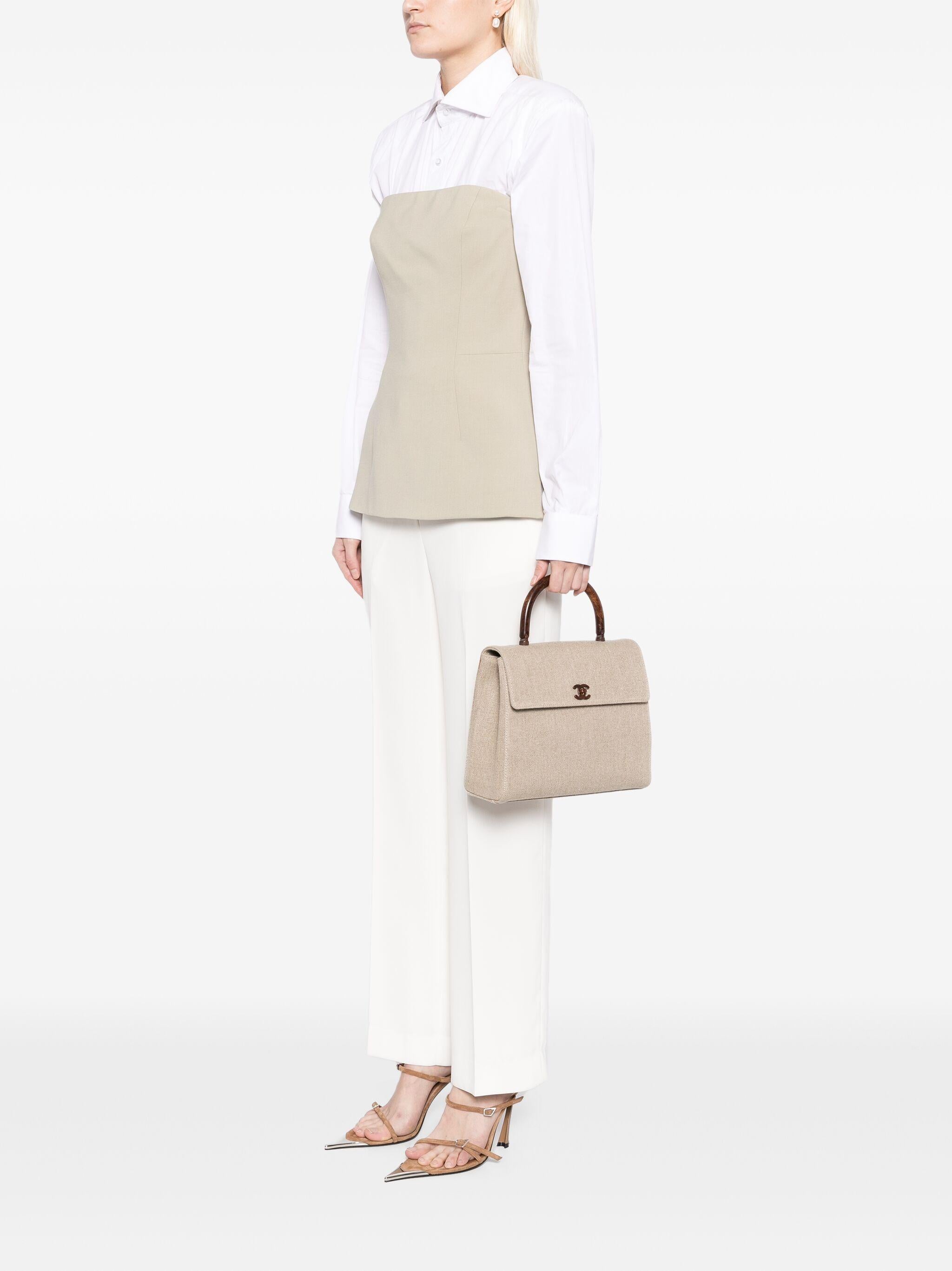 Chanel Bolso Kelly Mediano con Solapa de Lino y Asa Superior de Madera Falsa

Año: 2001 {VINTAGE 23 Años}

Cuerpo de lona de lino beige 
El asa y el cierre giratorio tienen aspecto de madera pulida 
Cierre de solapa y bloqueo de giro CC 
Herrajes