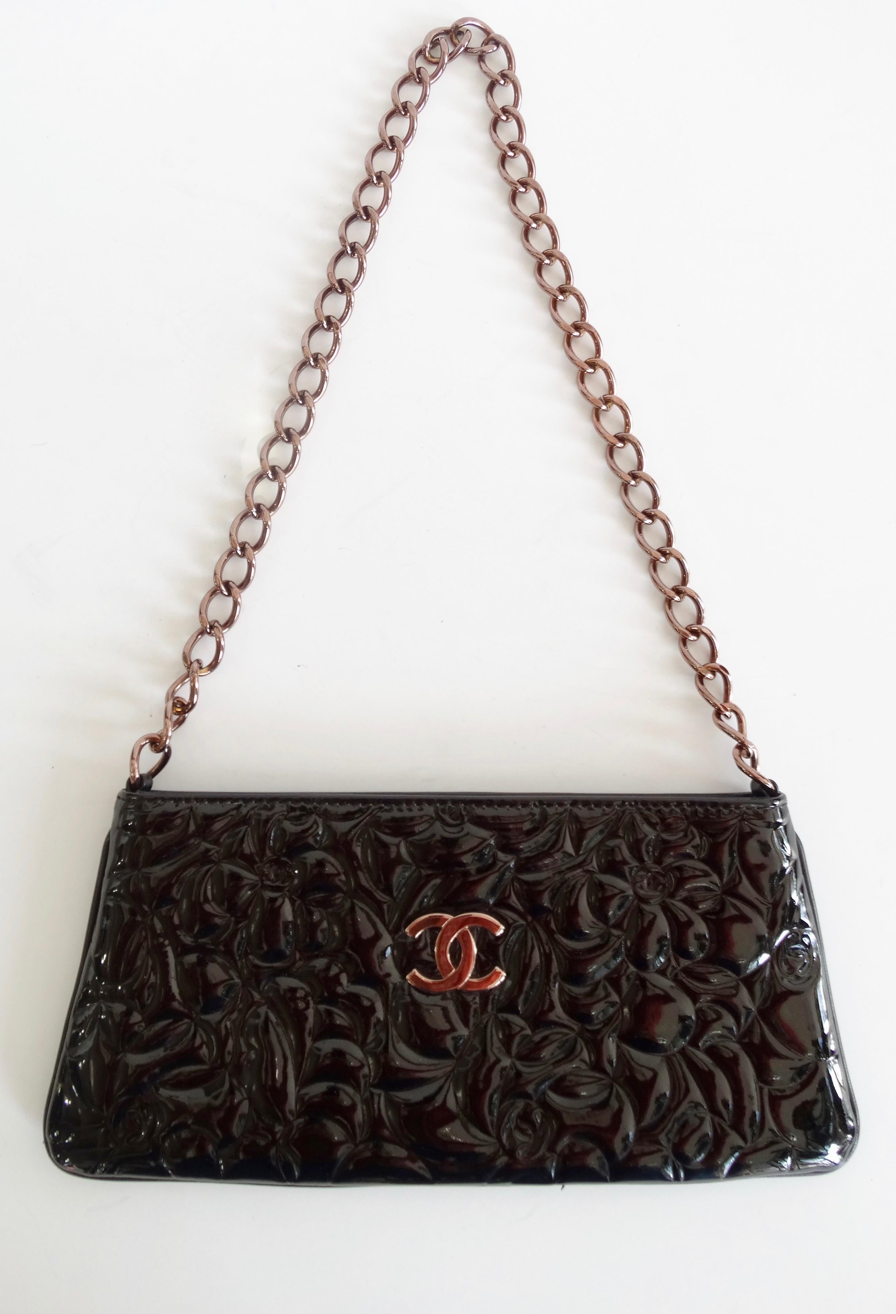 Complete your collection with this adorable Chanel bag! Circa 2003/2004 and made of back patent leather, this Chanel pochette is embossed with the iconic Camellia flower and small 'CC's. Front face features a bronze rose CC and chain link strap.