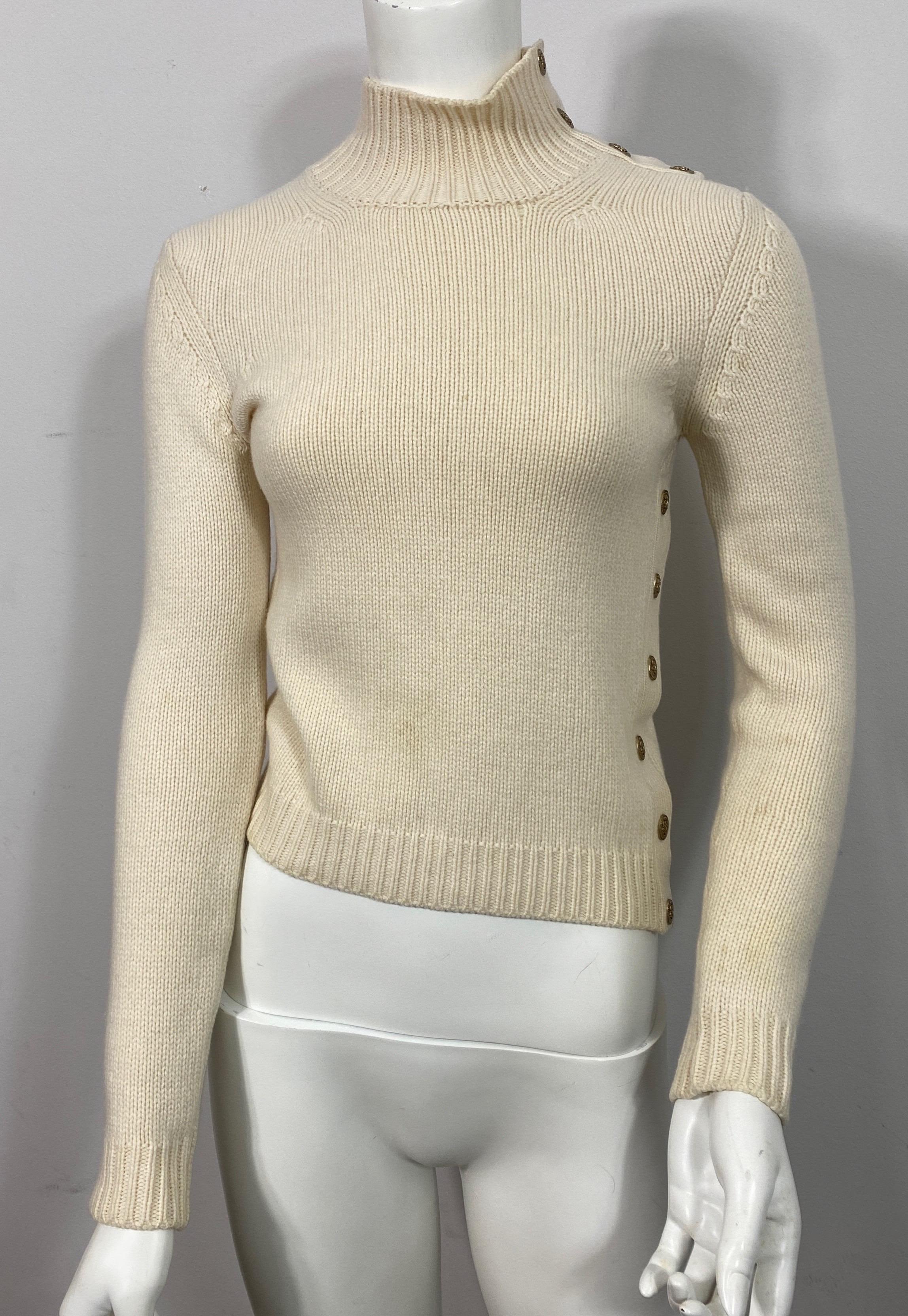 Chanel ivory cashmere knit sweater with logo snaps 2004A -Size 36

This classic early 2000’s chanel cashmere sweater is gorgeous. It is has a simple knit with a cable knit detail on the bottom, end of sleeve and the semi turtle neck. The neck has 4