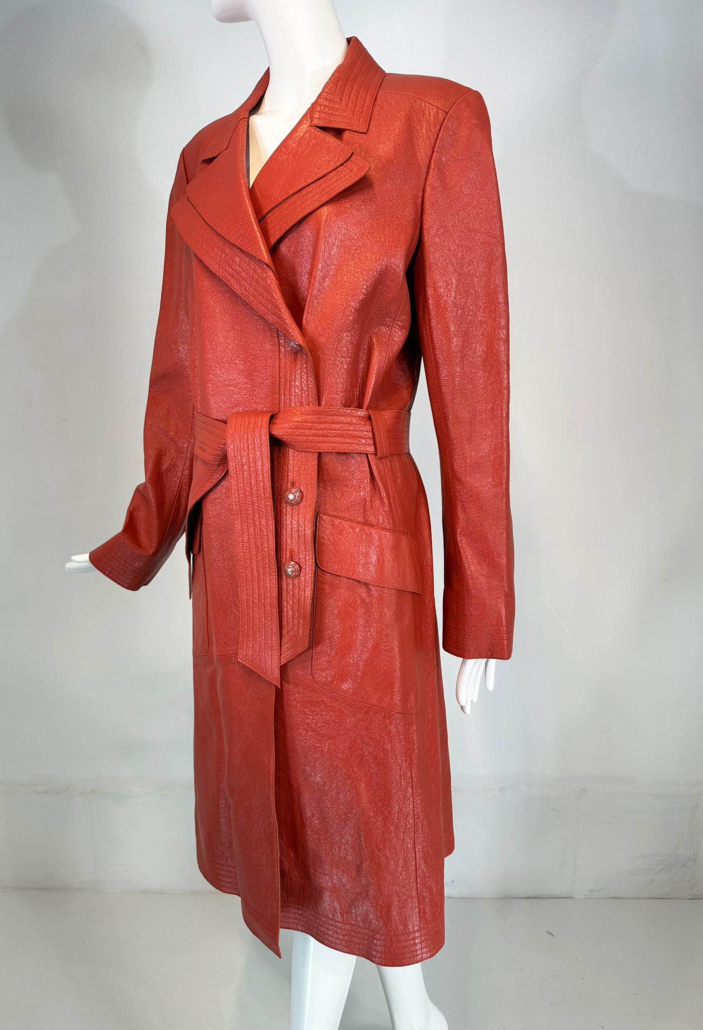 Chanel 2004P ziegelroter, glasierter Ledermantel mit Gürtel und Emailleknöpfen, Größe 44. Ein wunderschöner ziegelroter Farbton, der mit vielen Details versehen ist. Der langärmelige Mantel hat silberne Emaille-Knöpfe mit Logo an den Manschetten.