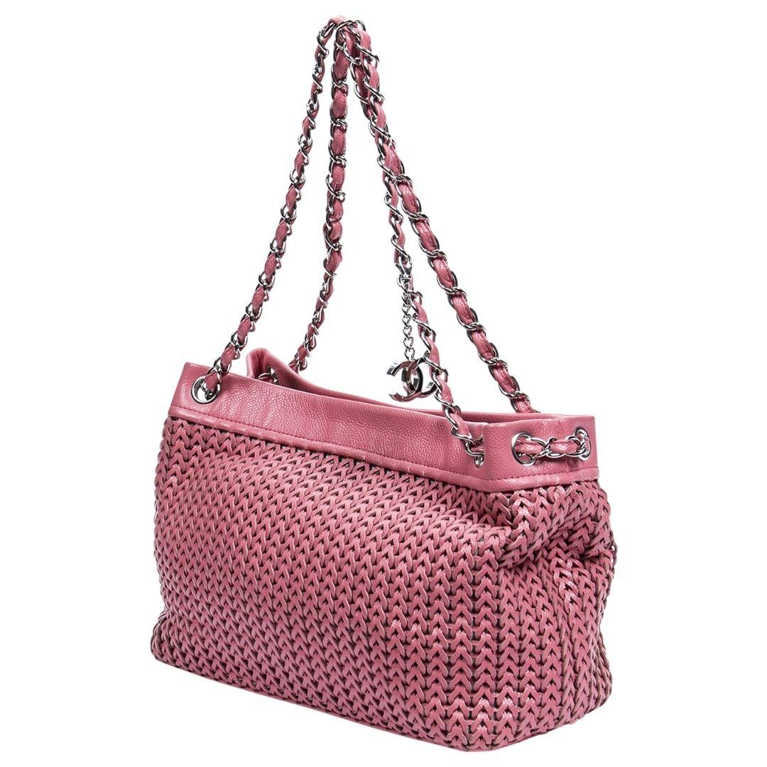 Pretty in Pink! This Chanel beauty is detailed in pink woven lambskin leather, silver-tone hardware, interwoven shoudler straps, CC charm and protective feet at the base. The magnetic snap closure opens to the fashion house's logo jacquard lining