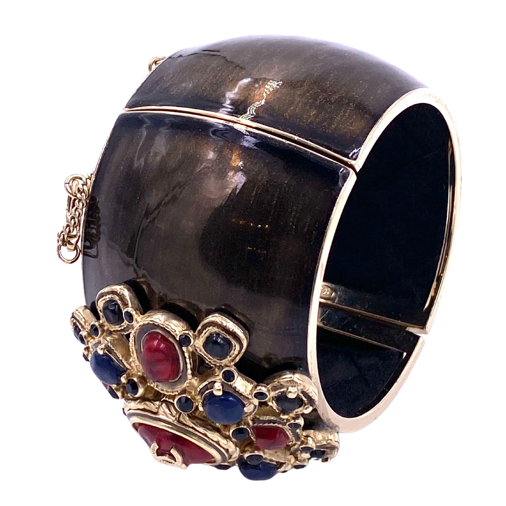 This Chanel 2006 cuff boasts a striking Maltese Cross design, accented with vibrant red and blue stones and intricate gold outlining. Elevate any outfit with this statement piece, perfect for adding a touch of luxury and sophistication. Expertly