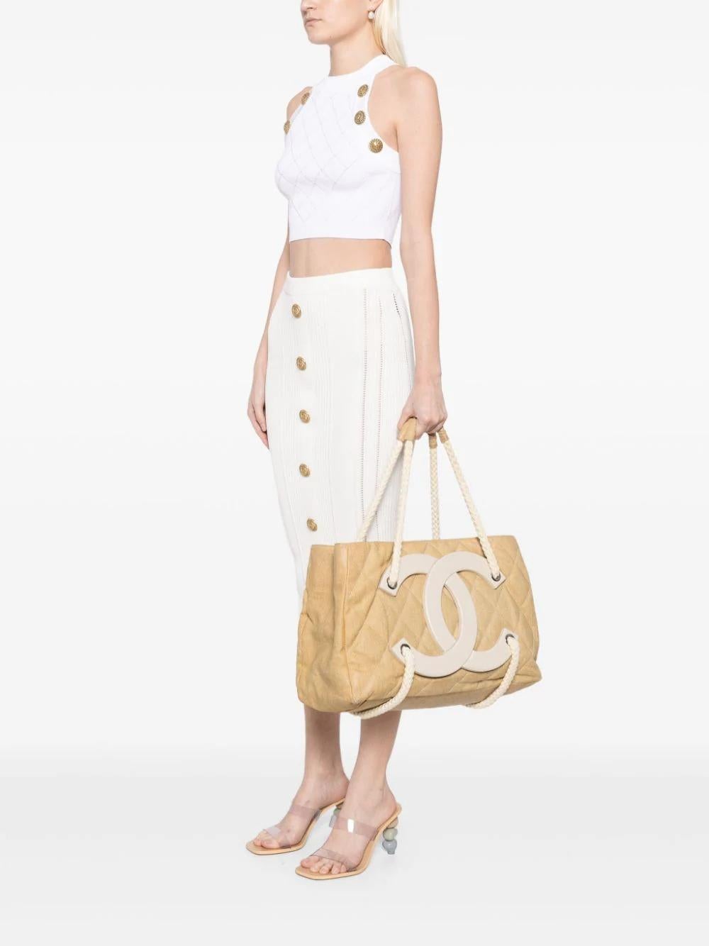 Diese wunderschöne, seltene Chanel Cruise Tote besteht aus beigefarbenem, beschichtetem Canvas, geflochtenen Griffen, einem oben offenen Design, einem Hauptfach mit Reißverschlussfächern, einer rautenförmigen Steppung, silberfarbenen Beschlägen und