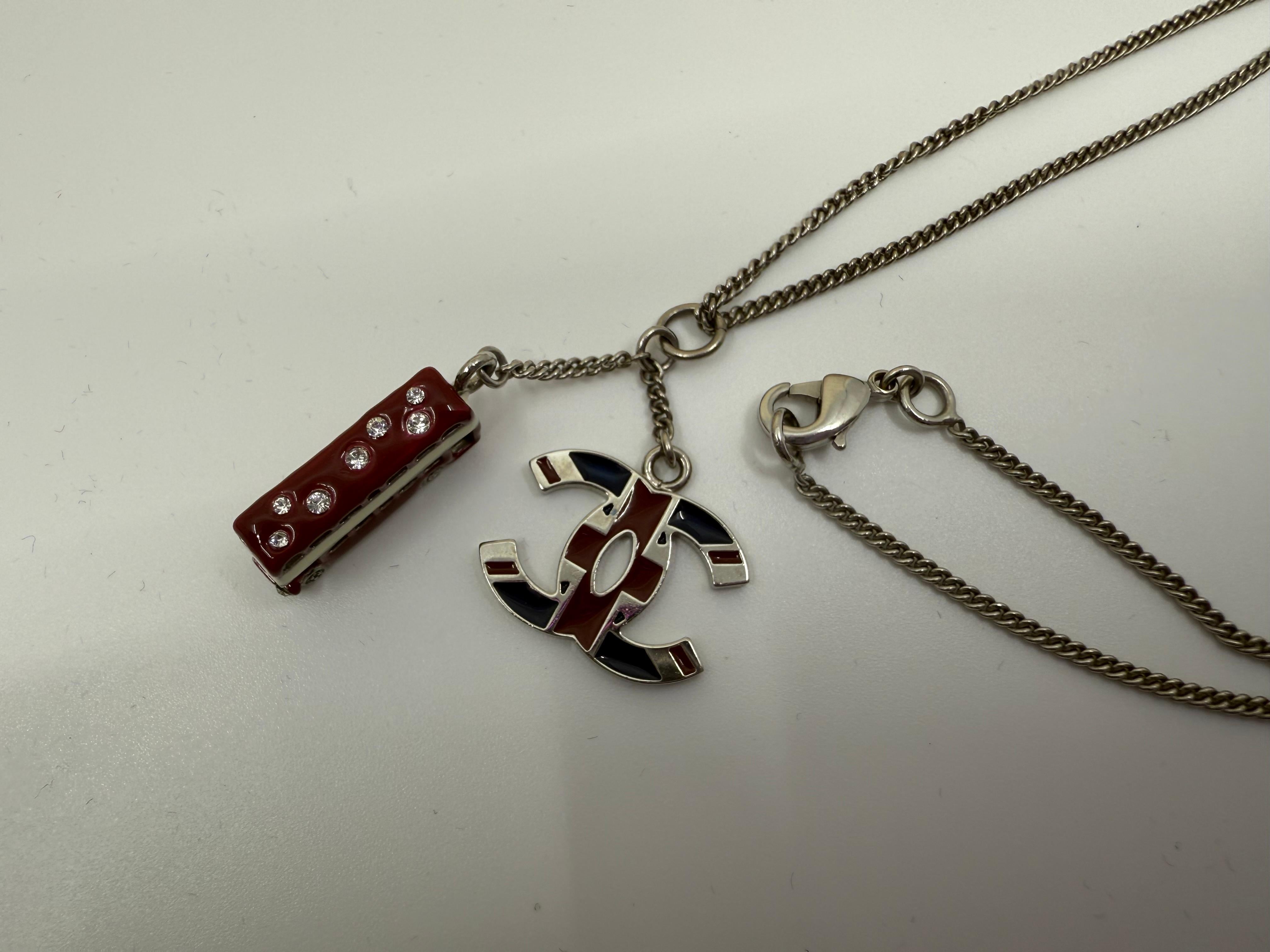 Un'affascinante e rara collana Chanel della collezione primavera 2008, caratterizzata da un ciondolo rosso smaltato a forma di autobus a due piani di Londra e da un logo patriottico Union Jack CC. Entrambi i charme sono appesi a una catena color