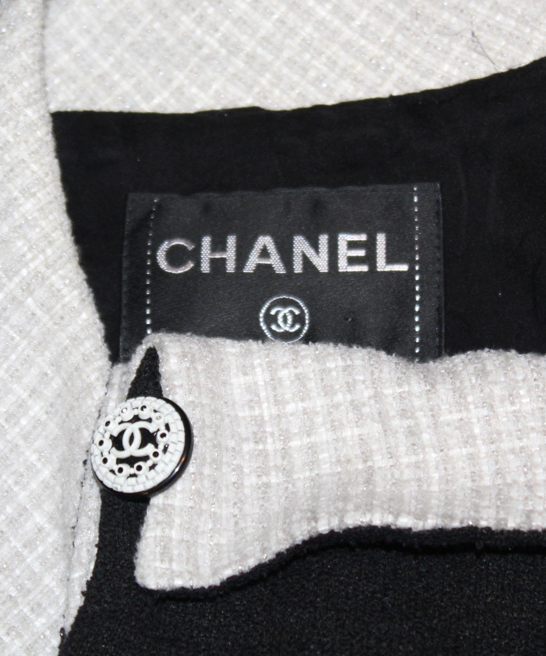 Chanel 2009 tweed wool blend black and ivory dress features silver threads throughout ivory color fabric.  This Chanel tweed sleeveless dress has a black tweed bow across bust line contrasting with the ivory fabric.  The dress has a drop waistline,