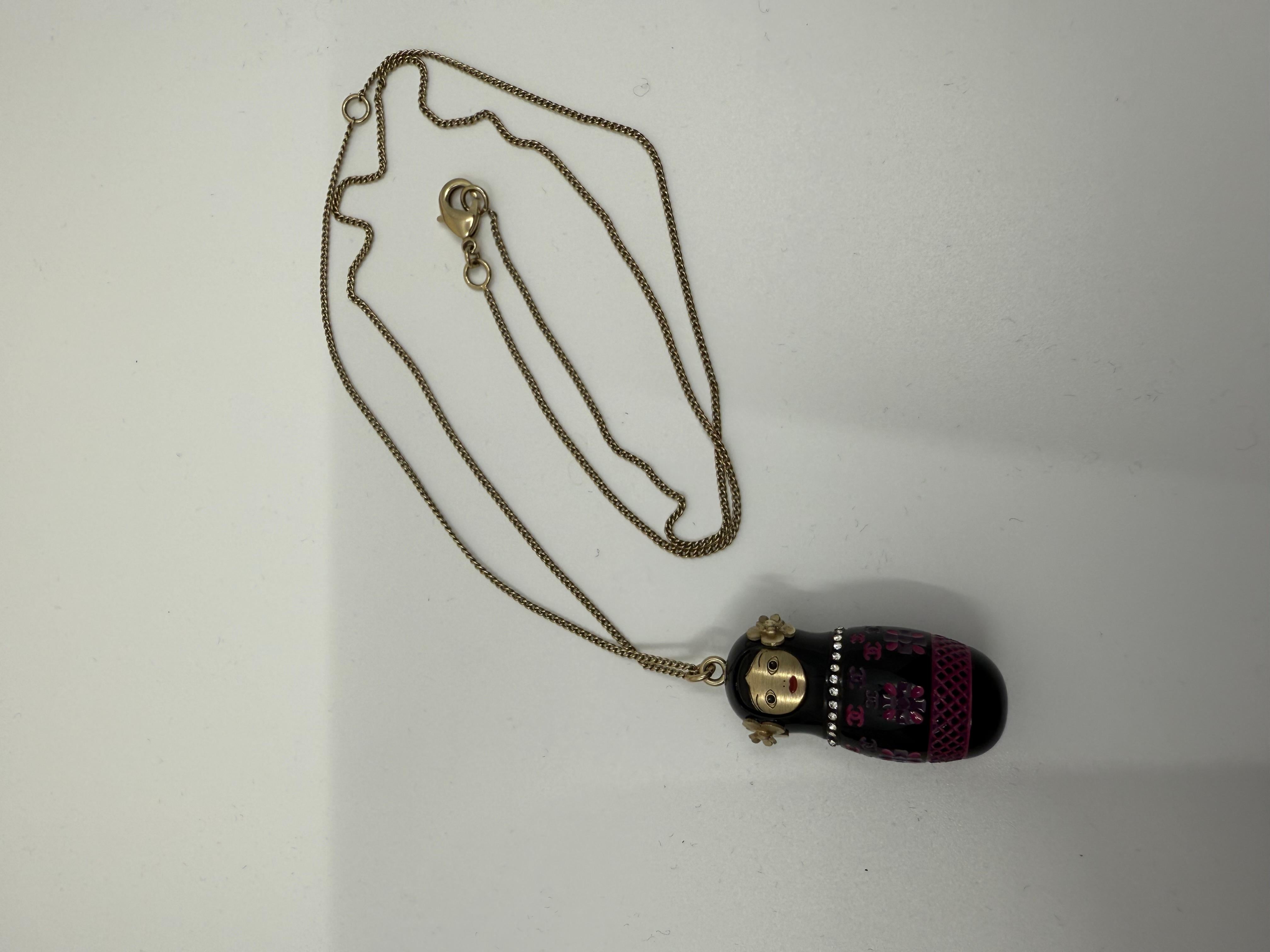 Raro e stravagante pezzo da collezione della Collection'S 2009 di Chanel, questa incantevole collana presenta un piccolo ciondolo a forma di bambola russa Matryoshka. Splendidamente dipinta a mano in smalto nero e fucsia con dettagli floreali e logo