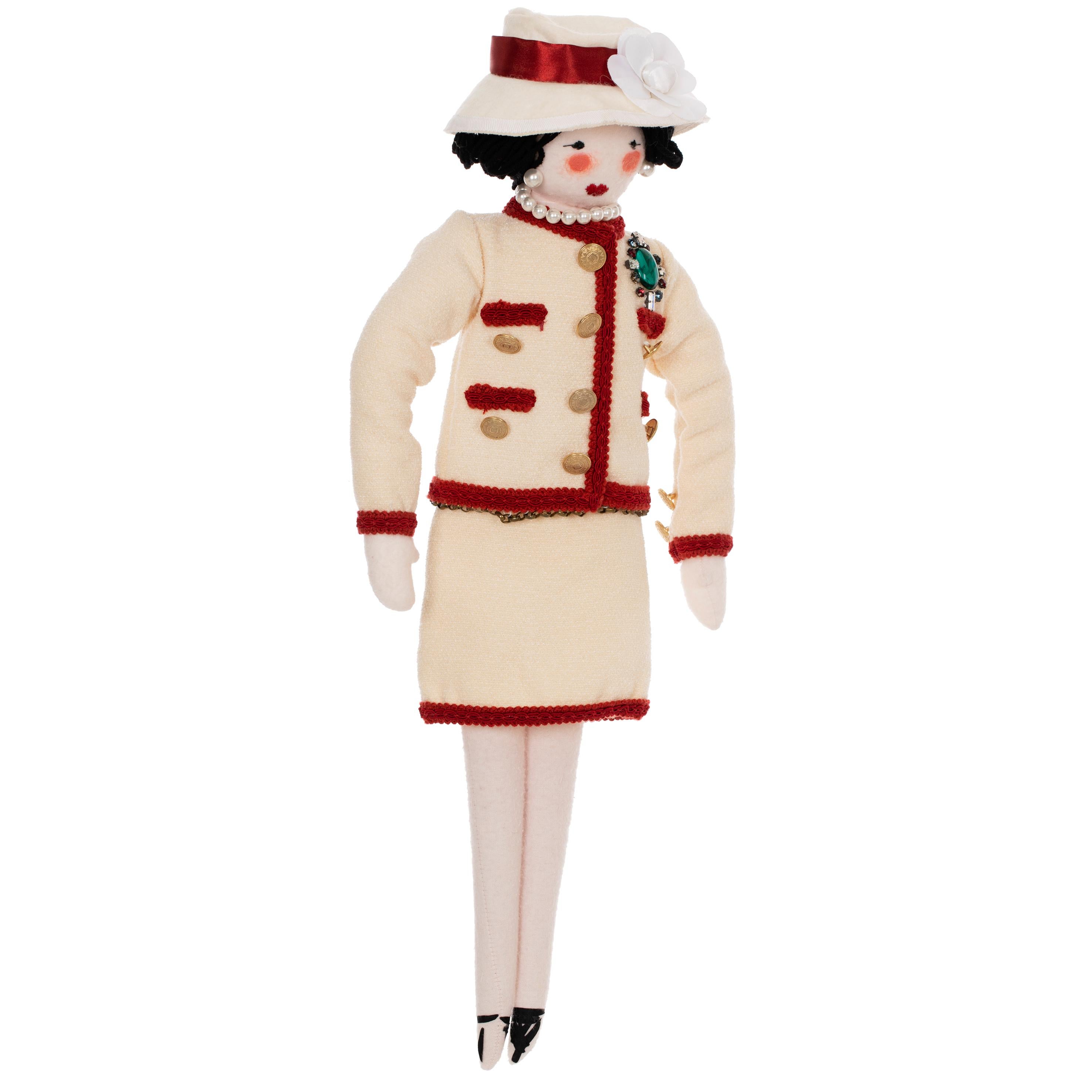 Cette poupée de chiffon classique Mademoiselle Coco de Chanel rend hommage à la fondatrice de la marque, Gabrielle 'Coco' Chanel. Fabrice en coton, la poupée est vêtue d'un tailleur jupe sans col caractéristique des années 60 qui incarne l'élégance