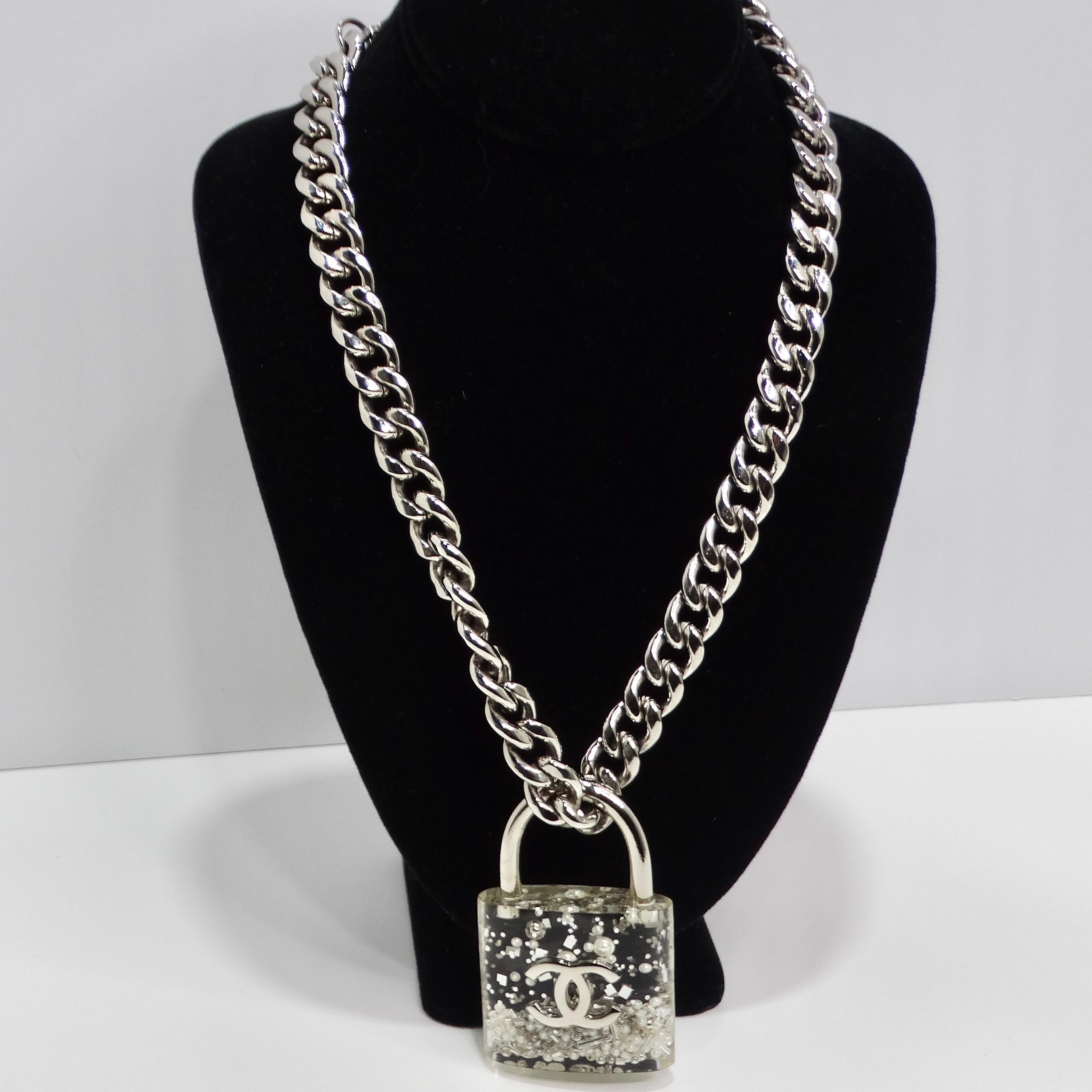 Introducing the Chanel 2014 CC Plexiglass Padlock Necklace, a bold and playful statement piece that exudes luxury and sophistication. This thick silver-tone chain necklace features a large plexiglass padlock filled with silver-tone beads and faux