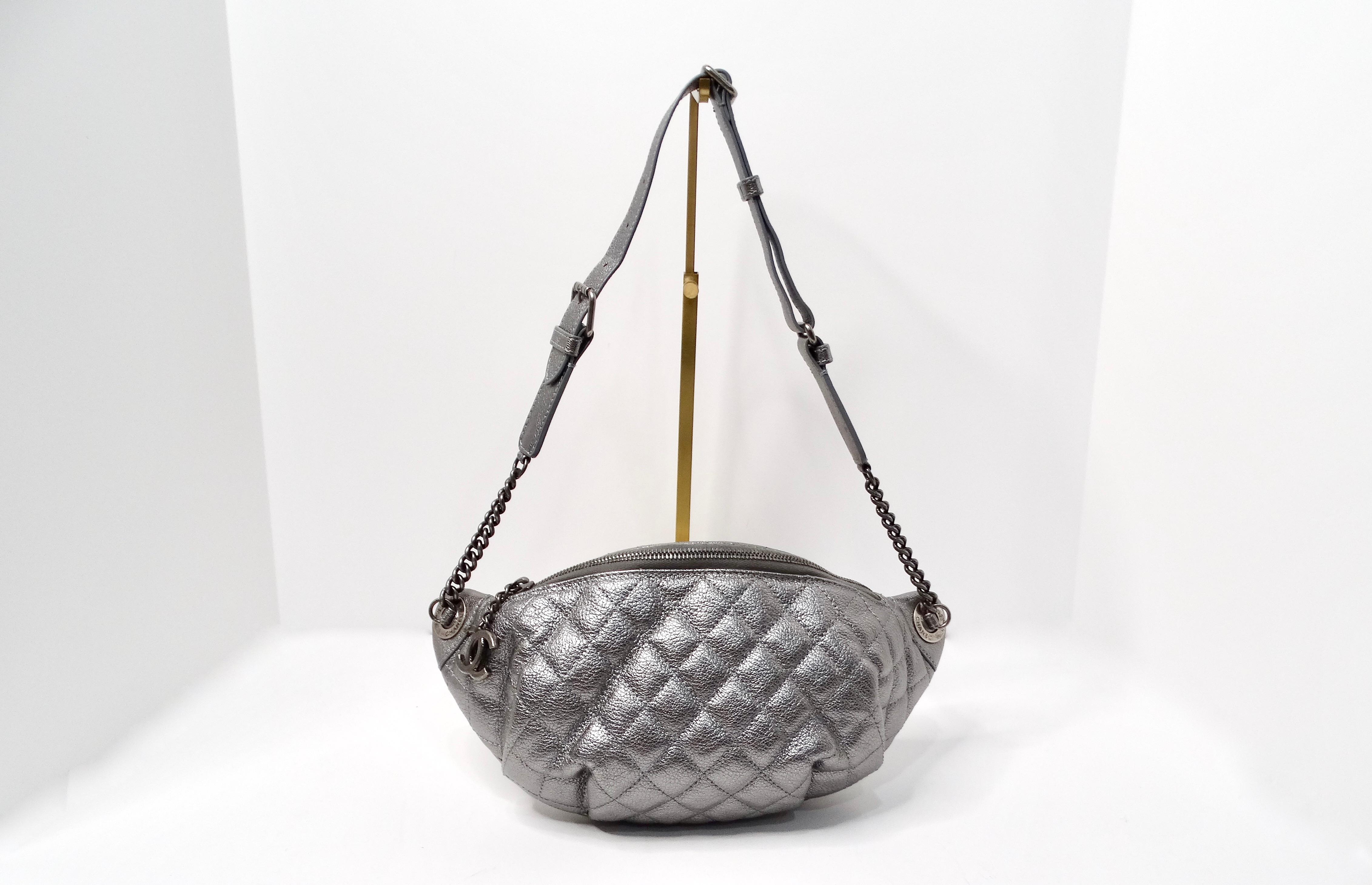 The Chanel 2015 Silver Metallic Quilted Calfskin Banane Fanny Pack Waist Bag is a perfect fusion of style and practicality, reflective of Chanel's luxe aesthetics. Crafted from shimmering metallic calfskin leather, this fanny pack exudes an