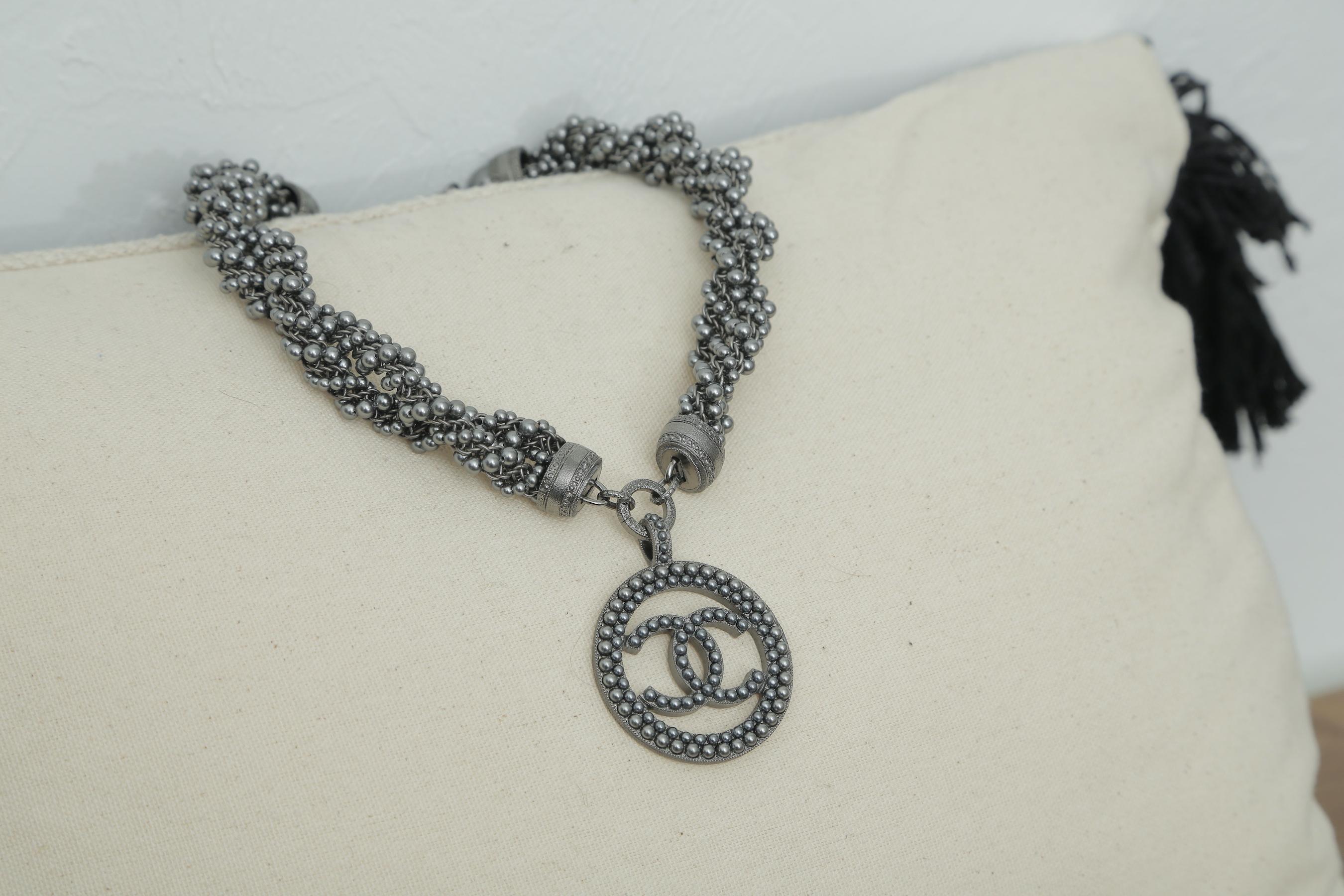 Chanel grey beaded crystal CC chain choker with CC medallion pendant. This bold choker necklaces features multiple strands of faux dark pearls braided together. There is a large CC pendant at the front center and a smallCC dangling charm at the