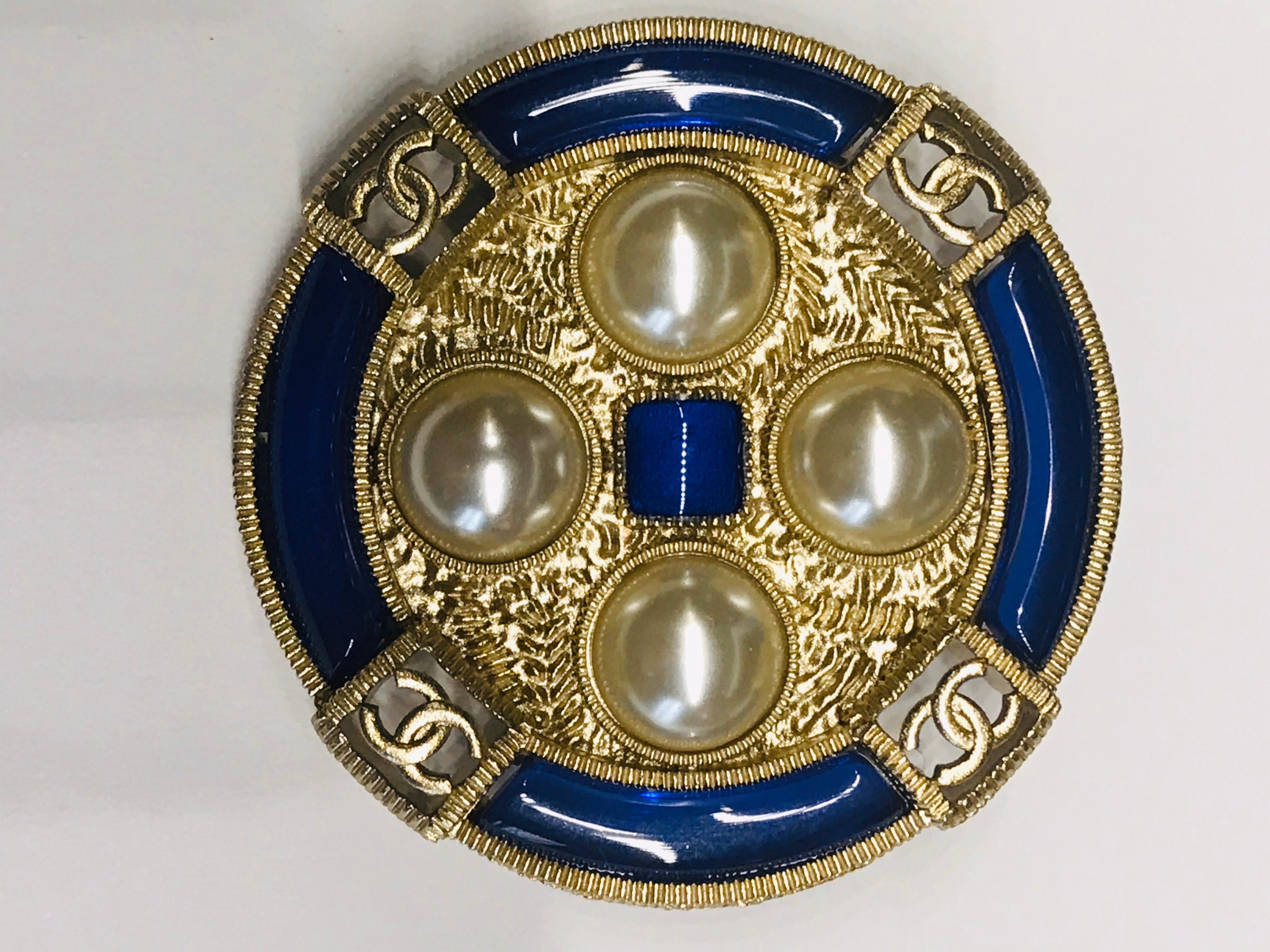 A lovely light gold, faux pearl cabochon and blue lucite pin with four cut out interlocking CC logos. The pin is 1.75” in diameter and has the oval Chanel signature plaque on back. It is inscribed “Chanel with registry and copyright stamps, 19 on