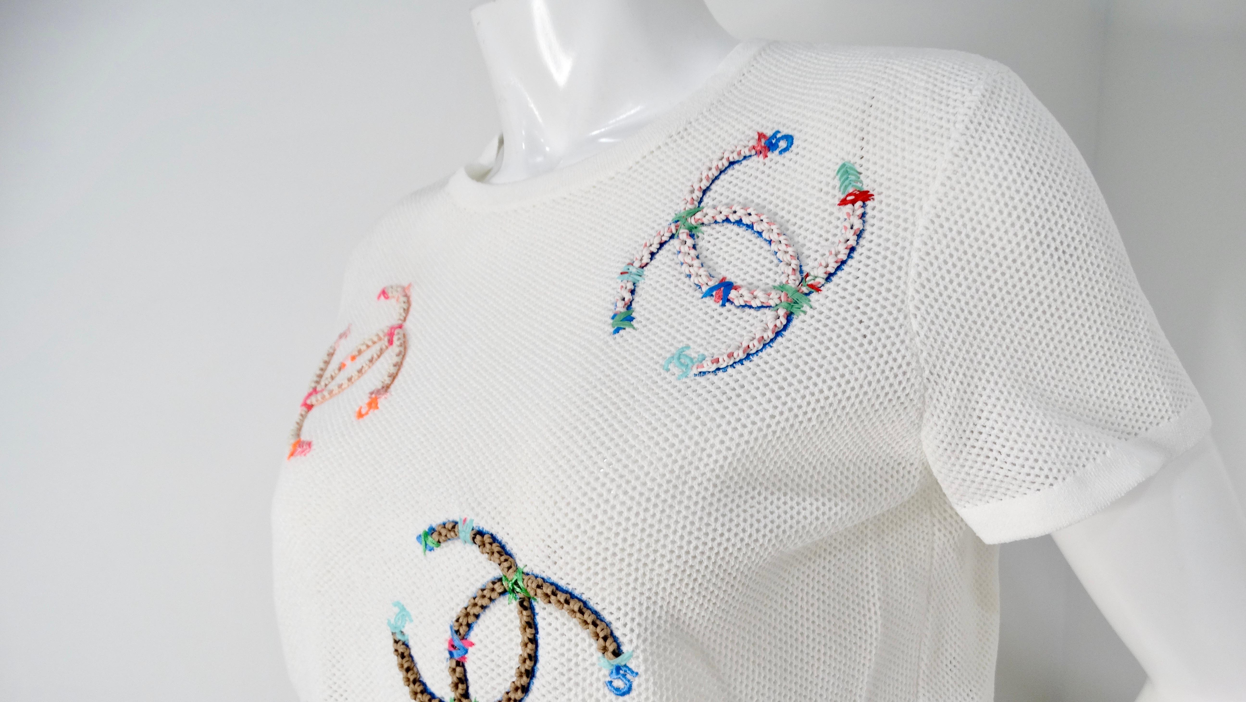 The Chanel 2019 White Mesh Embroidered Colorful Interlocking CC Logo T-Shirt is a striking blend of playful elegance and contemporary style. This cropped beauty features a stunning array of large, embroidered interlocking CC logos, artfully rendered