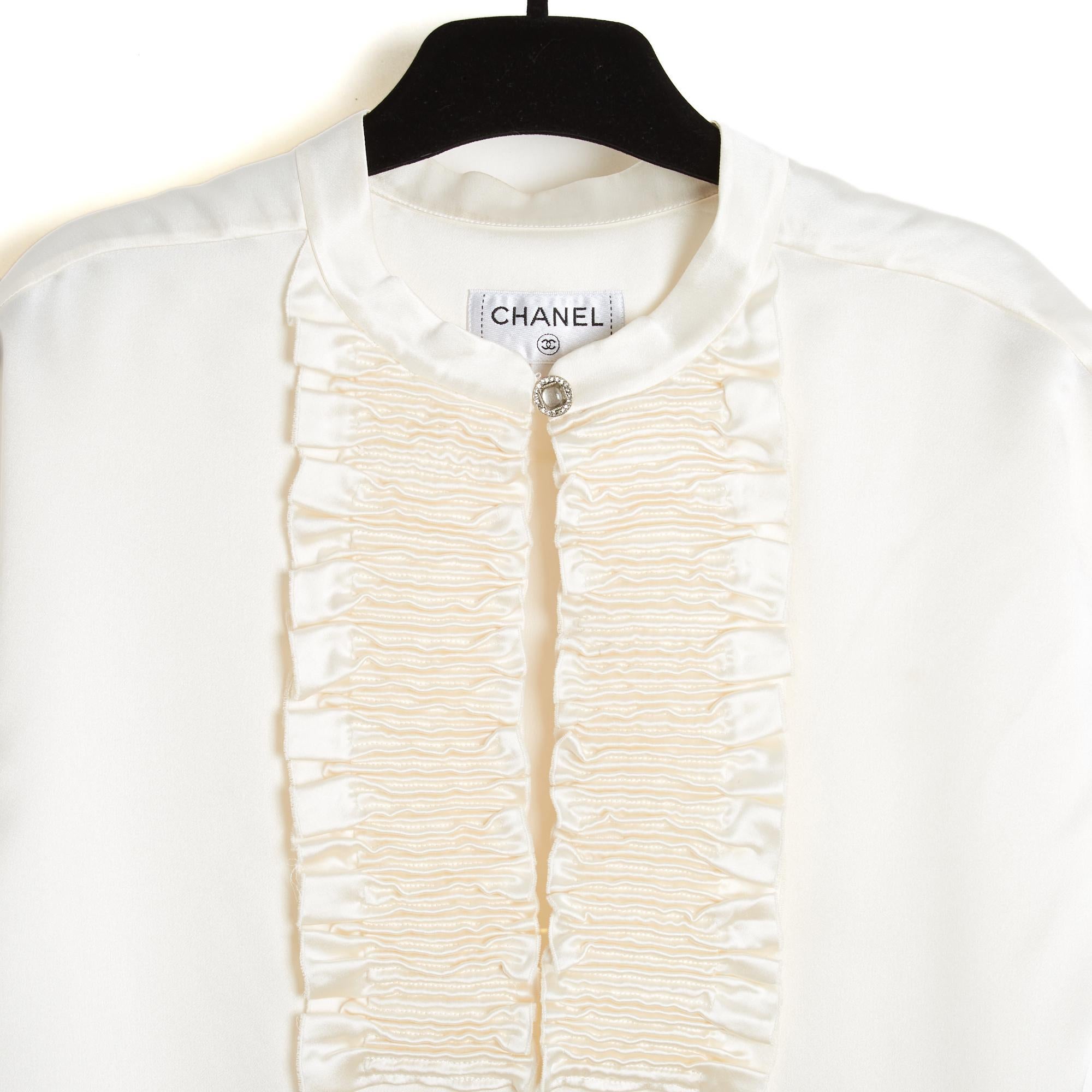 Blusa Chanel circa 2020 de satén de seda color crudo, sin mangas, corte oversize, pechera fruncida en un escote profundo cerrado por un botón joya. Talla 40FR o UK12 y US10: 45 cm de hombro, 49 cm de pecho, 70 cm de longitud. Falta la etiqueta de