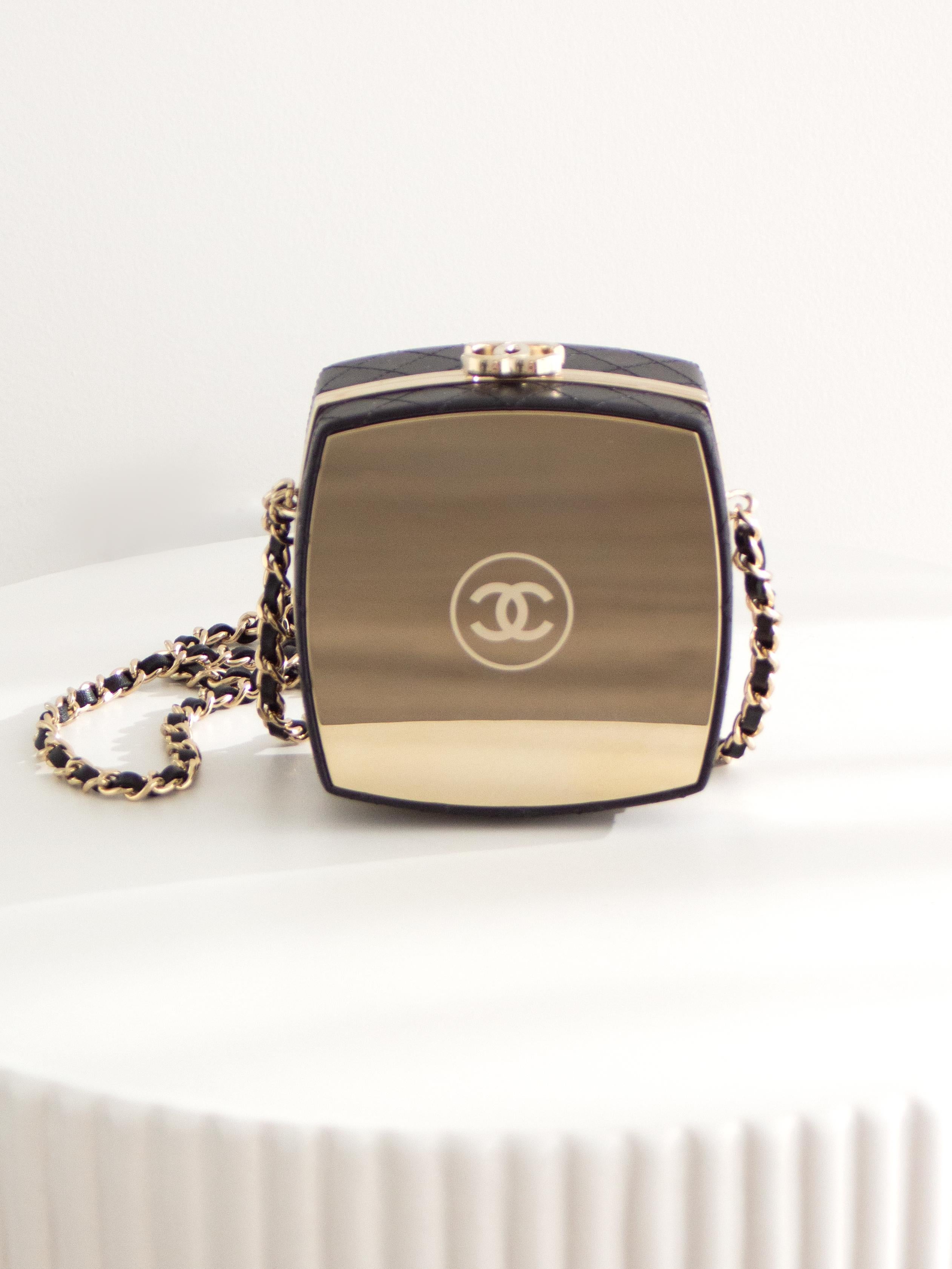 This is the Chanel 2021 Beauty Box clutch bag, a stunning and rare piece from Chanel's 21K collection. The bag features a unique compact powder case-inspired design, combining luxurious quilted black lambskin leather with striking gold-tone metal