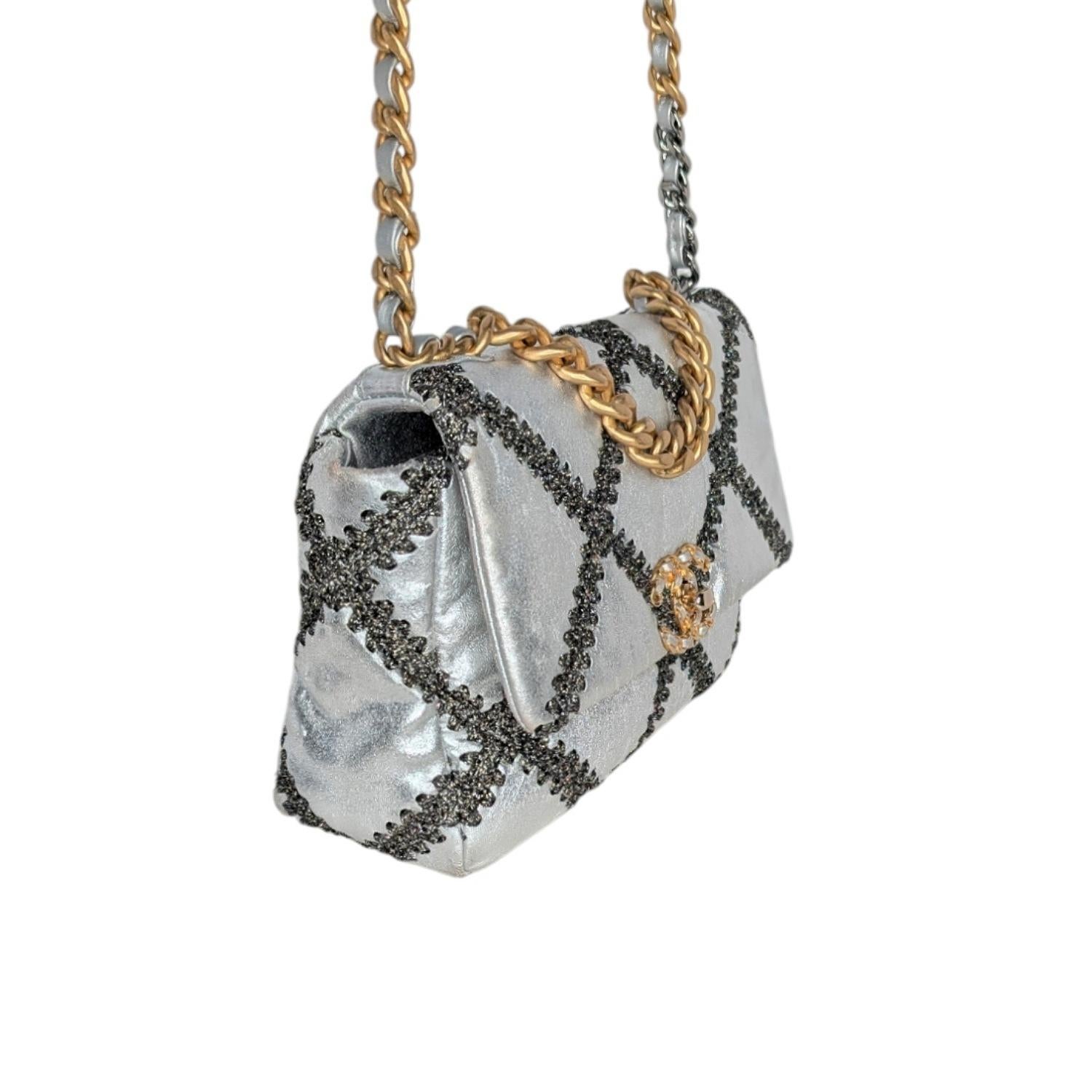 Chanel Metallic Calfskin Crochet Medium Chanel 19 Flap in Silver. This pillowy soft shoulder bag is crafted of oversized quilted leather in silver with black stitching. The refined bag features a chain detail CC turn-lock on the flap, a magnetic