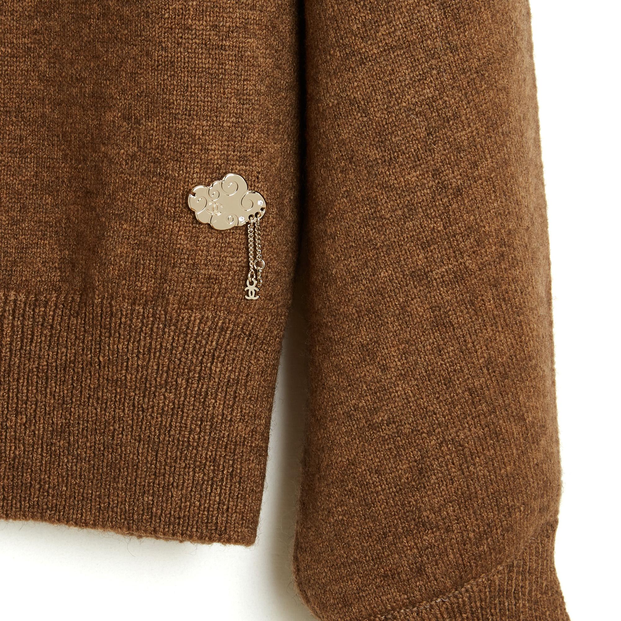 Jersey de la colección Chanel 2025 (en curso) de cachemira marrón medio con un sutil efecto jaspeado. Presenta una silueta oversize ligeramente recortada, cuello redondo, mangas globo (anchas en el codo y fruncidas en la muñeca), ribete de canalé en
