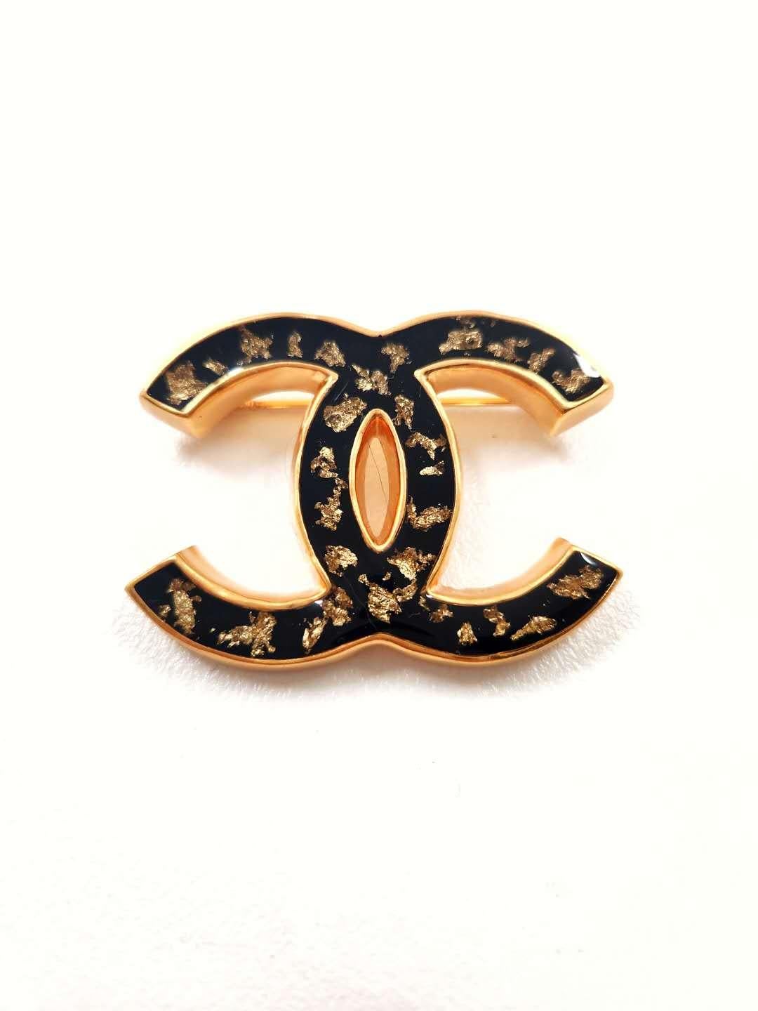 Introducing the Chanel 23 Gold Black Resin with Gold Foil CC Large Brooch, a stunning accessory that captures the essence of Chanel's timeless elegance and impeccable craftsmanship. This brooch is a true statement piece that exudes sophistication
