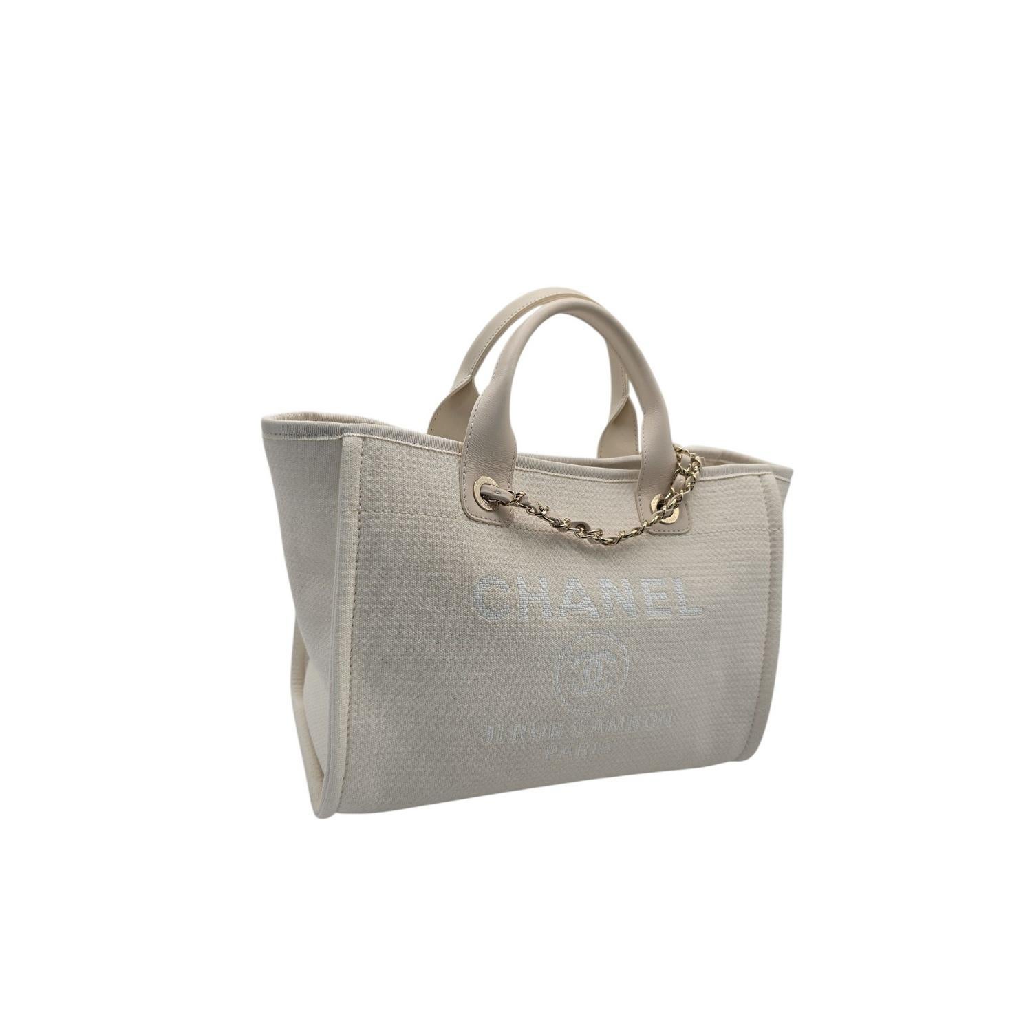 This stylish shoulder bag is crafted of tightly woven fibers in off white, with a Chanel Rue Cambon Paris logo on the front. The bag features beige leather handles, and fabric-threaded polished light gold chain link shoulder straps. The top is open