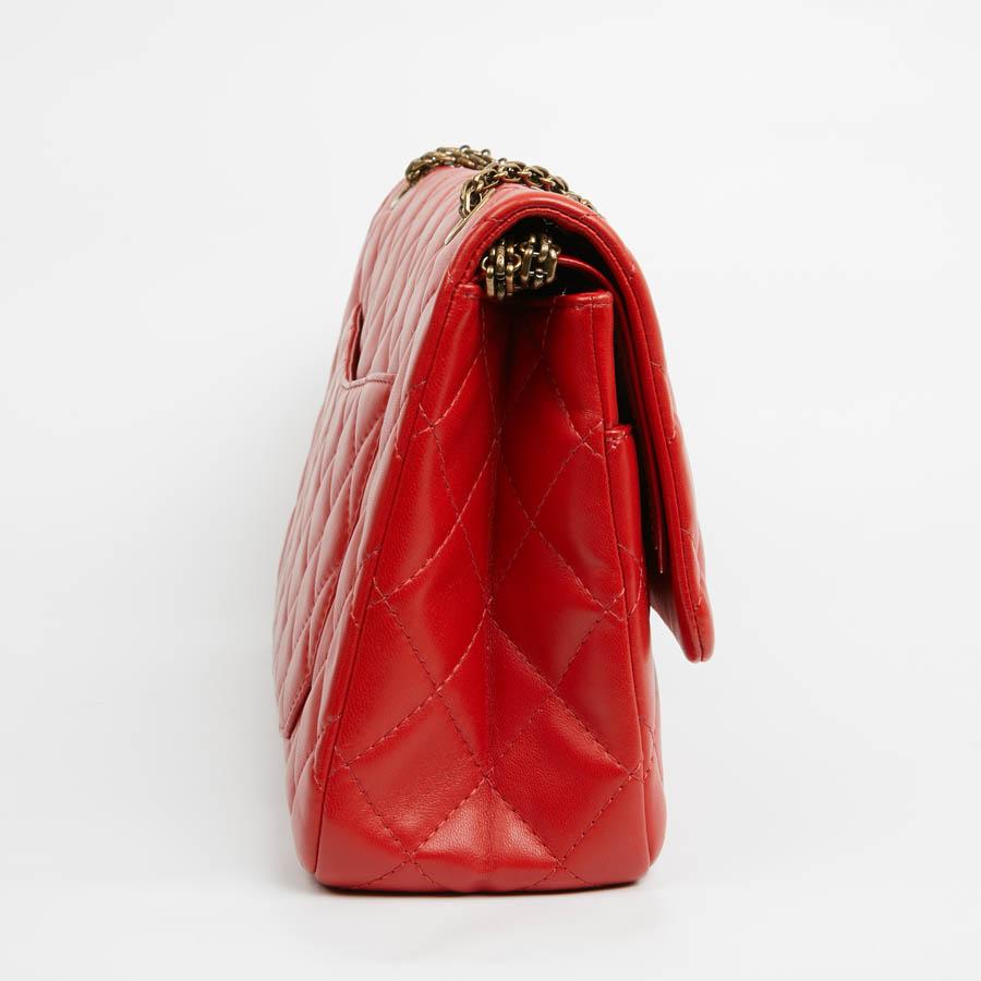Le mythique sac à double rabat 2.55 de la Maison Chanel est confectionné en cuir d'agneau rouge lisse et matelassé. L'intérieur est doublé de cuir rouge. Les bijoux sont cuivrés et vieillis. En très bon état, n'ayant pratiquement jamais été