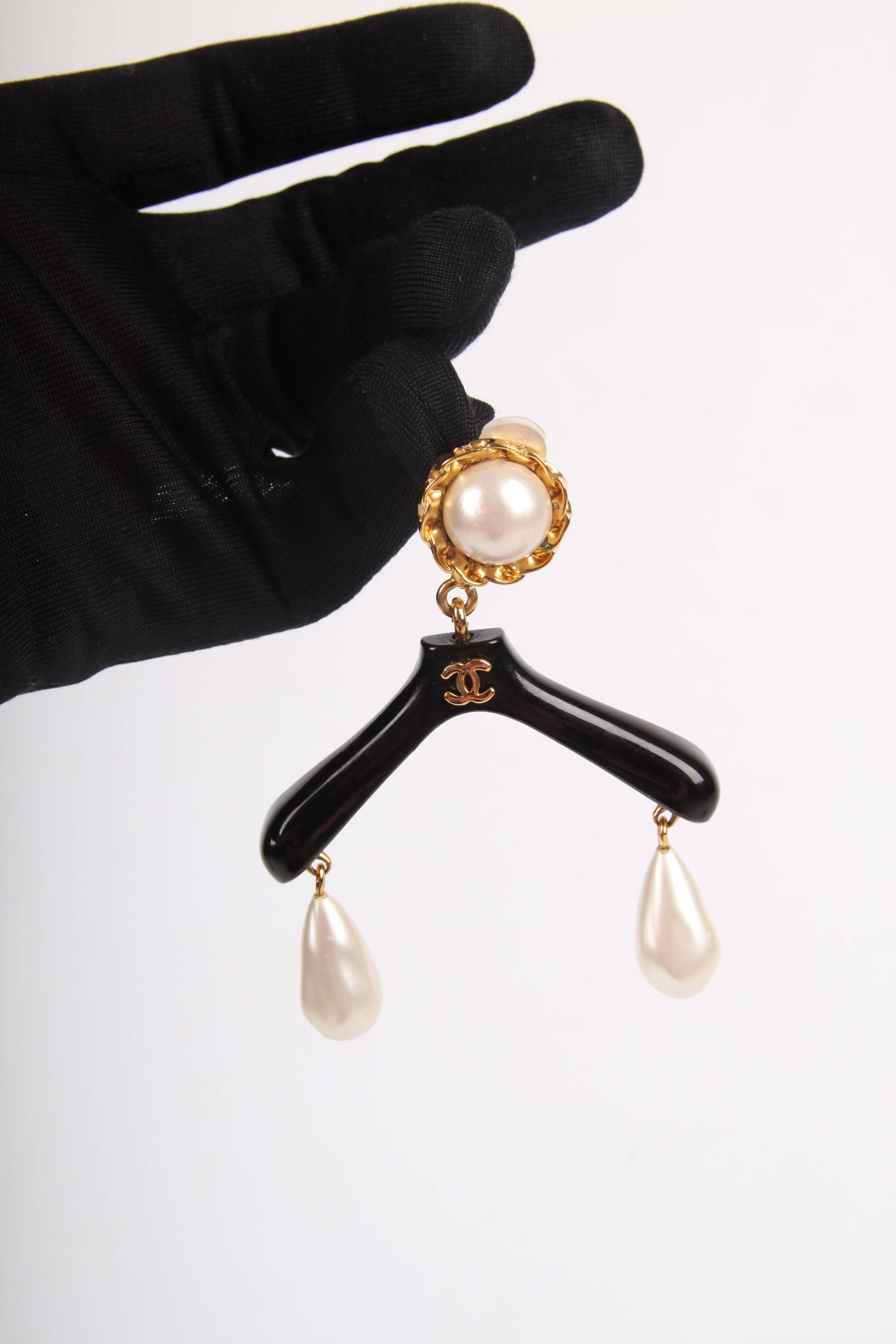 Very recognizable and super cool! Clip-on earring by Chanel in the shape of a coat hanger.

A large faux pearl on top with a gold-tone brim, you find the clip on the back. Underneath the black coat hanger with a golden CC logo in the center. On both
