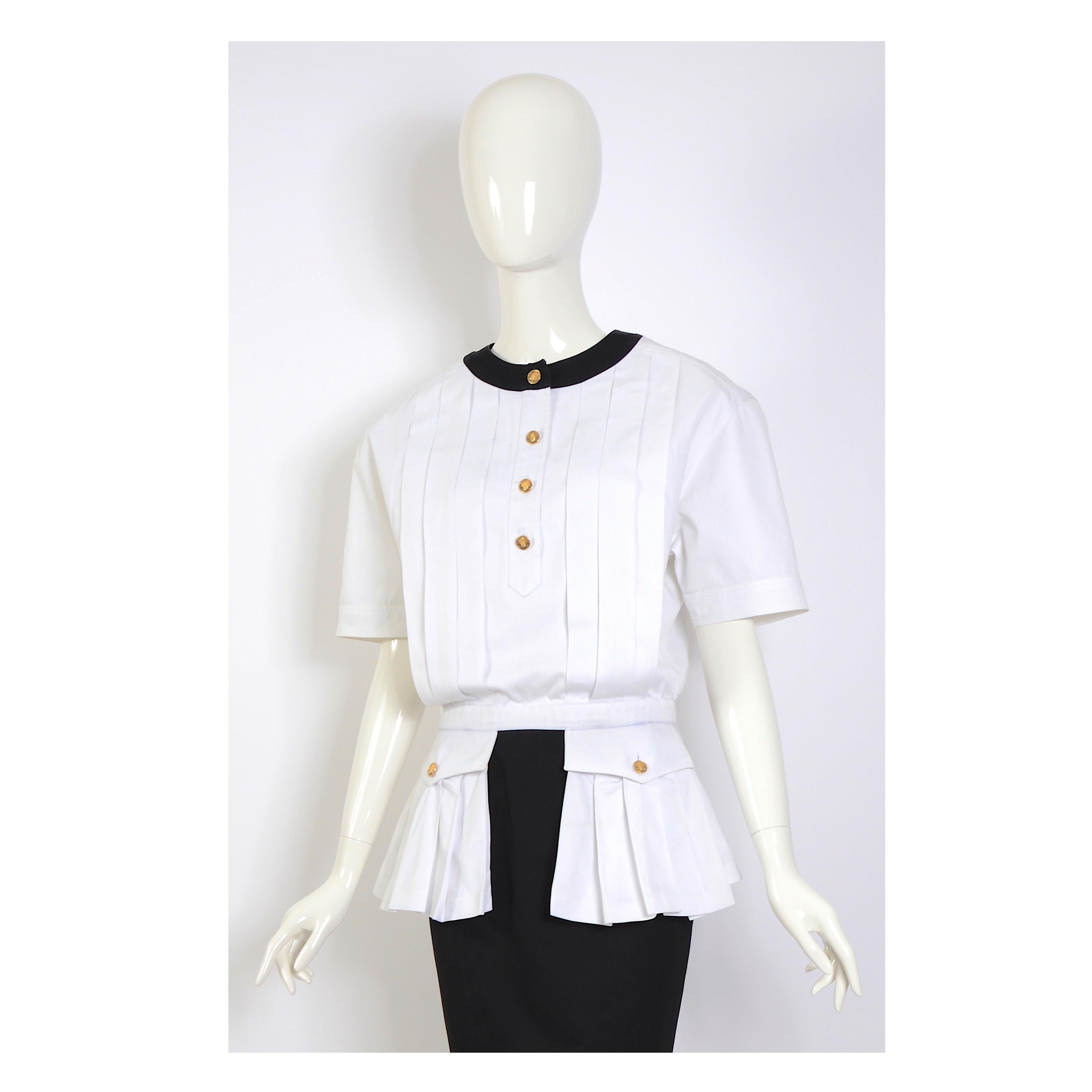 Robe Chanel en coton blanc et noir, col rond avec boutons dorés, manches courtes, plis sur le devant et poches plissées avec rabat et bouton.
Les larges épaulettes de la robe ont été retirées, mais il est possible de les remplacer si on le souhaite.