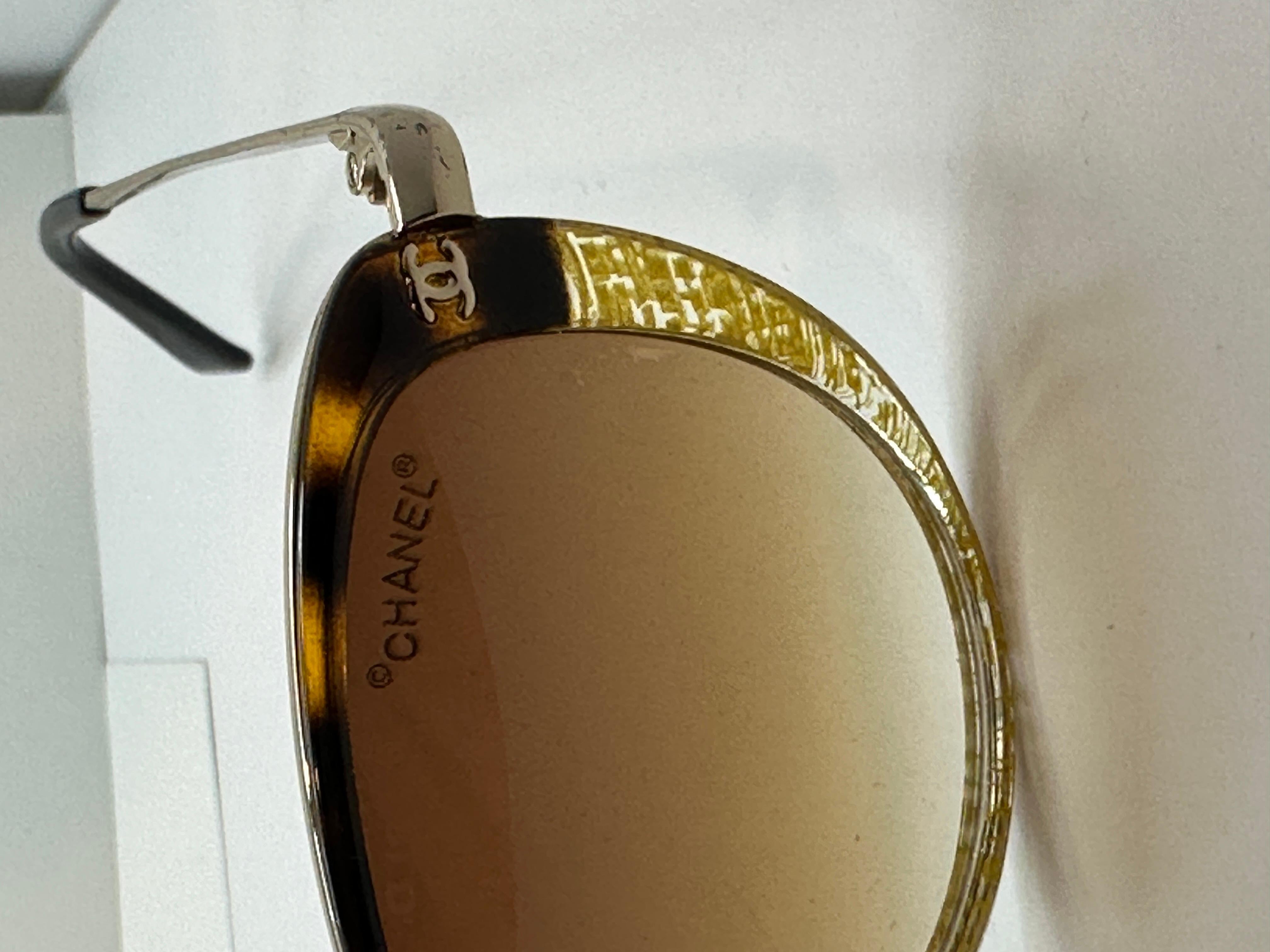 Chanel Sonnenbrille in abstraktem Gold und Schildpatt mit vergoldeter Hardware. Die Enden des Arms sind mit schwarzem Lucit verkleidet. Die Vorderseite misst 5 5/8 Zoll in der Breite, Höhe misst 1 7/8 Zoll, und die Arme sind 5 1/4 Zoll in der Länge.