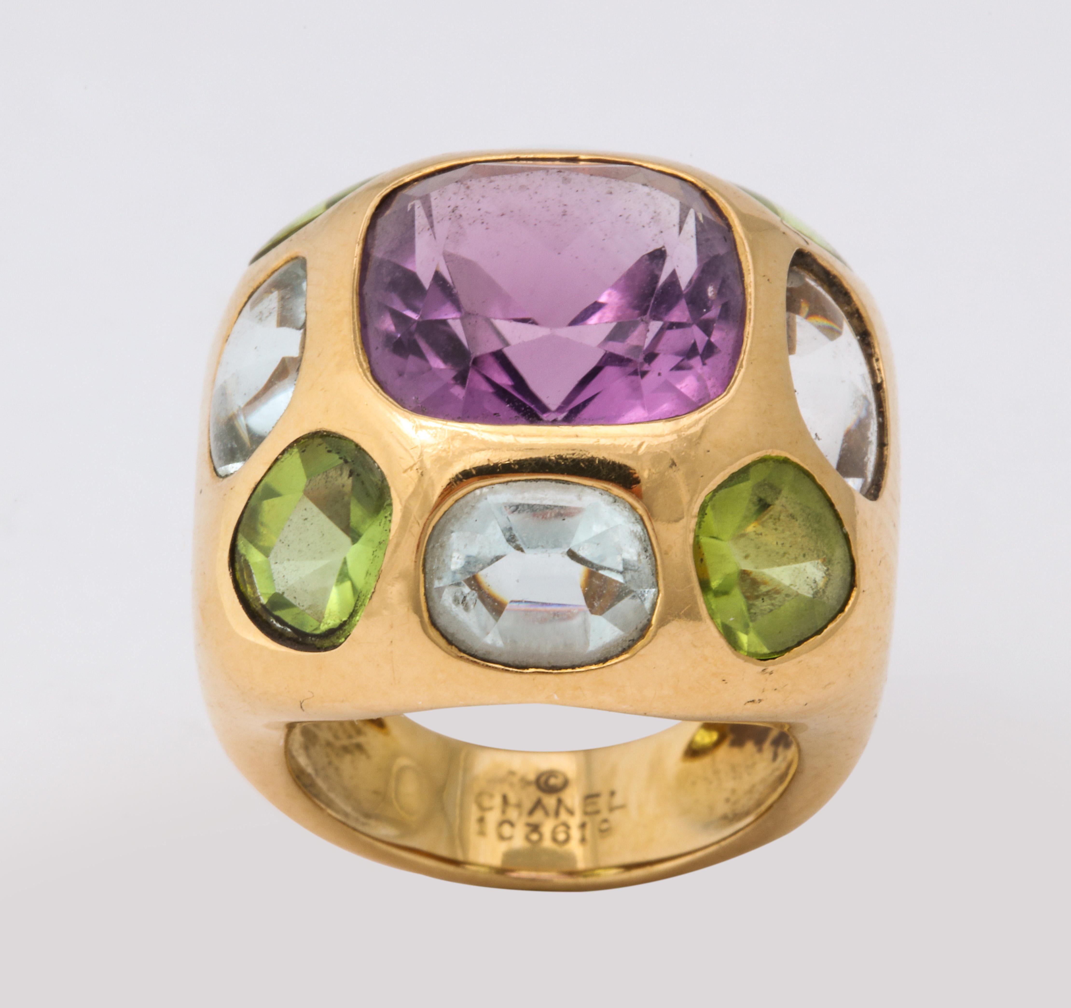 Iconic Chanel design circa 1990 featuring a central cushion cut rich, purple amethyst surrounded by aquamarine and peridot.  The surrounding stones are uniquely cut with buff top smooth surfaces.  Signed and numbered with proper French
