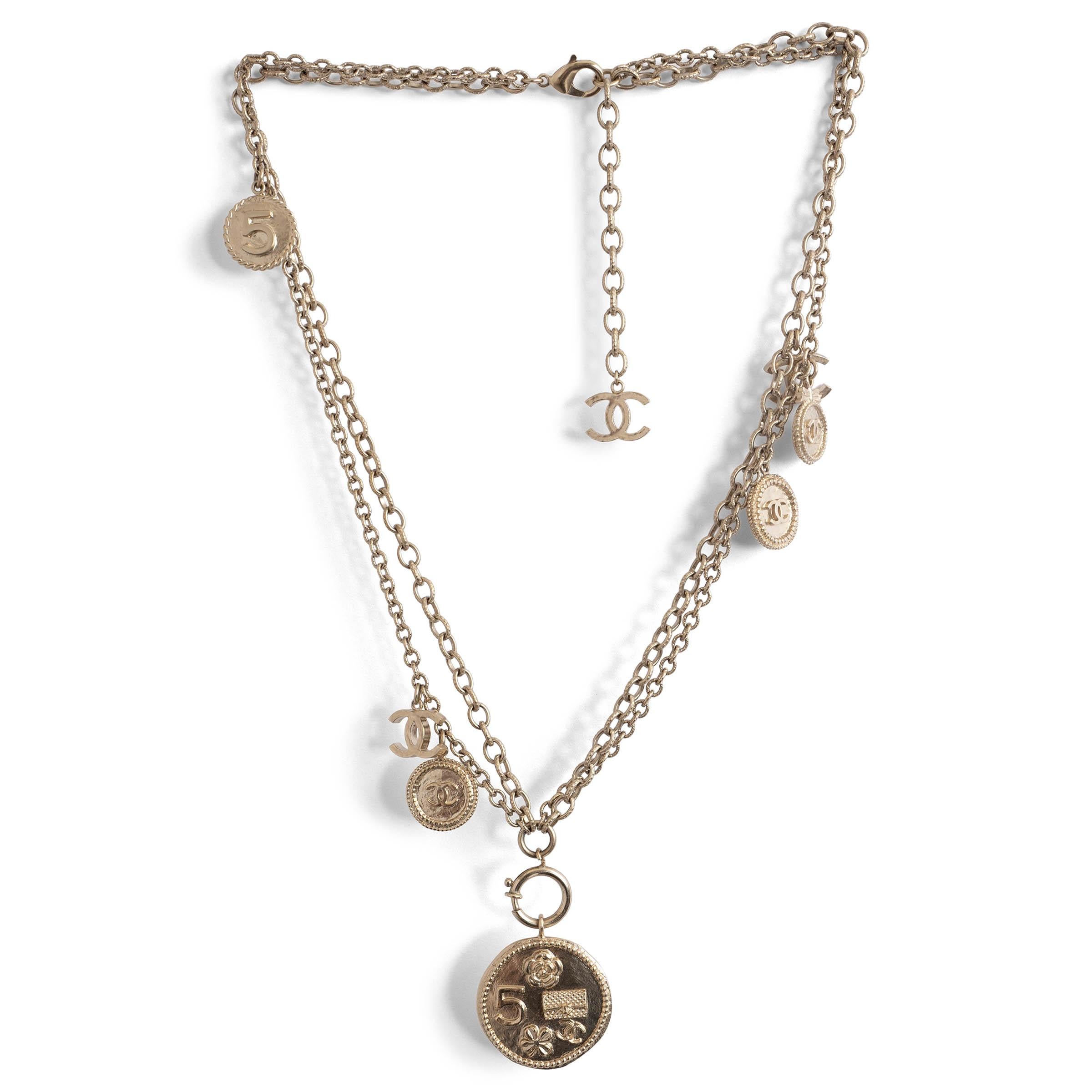 Questa collana a doppia catena 100% autentica di Chanel in tonalità argento antico presenta una serie di ciondoli con motivi iconici di Chanel, oltre a un sorprendente ciondolo a forma di moneta. Questo pezzo senza tempo offre eleganza e audacia,