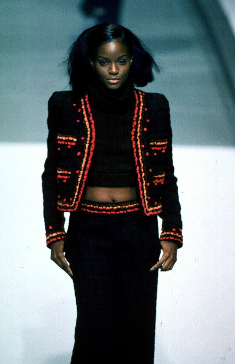 Incroyable veste Chanel de la collection Automne 1997. Boucle de laine marron chocolat agrémentée de bordures en chenille rose, orange, marron et bordeaux et de pompons en velours rose. La veste est sans col, légèrement raccourcie et ouverte. Un