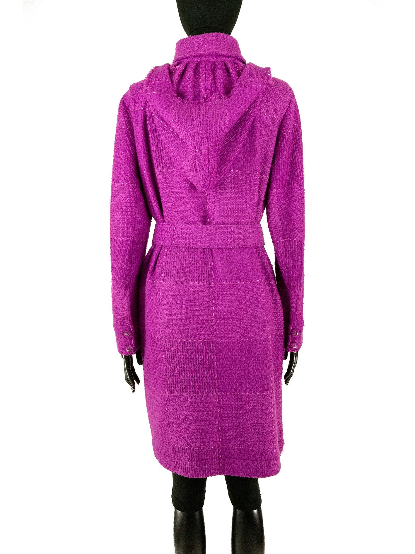 This Chanel tweed coat, hailing from the Autumn 2007 collection, is in a magenta pink with decorative stitching. The back features a hood attached to the standard collar. The silhouette is narrow and straight but can be made fitted with the