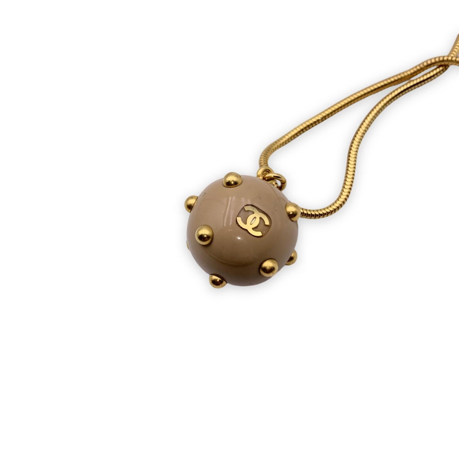 Gold metal chain necklace from CHANEL with beige Sphere. The Sphere is decorated with gold metal studs and small CC - Chanel logo.Snake chain with hook closure. Total length of the chain: 29.5 inches - 75 cm. 'CHANEL 00 CC A - Made in France' oval