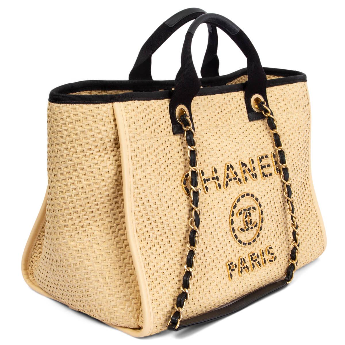 100% authentic Chanel Deauville Large shopping bag in natural beige woven raffia with black leather trimmings, grosgrain top edge and gold-tone hardware. The design features woven leather & metal chain logo appliqué on the front. Closes with a