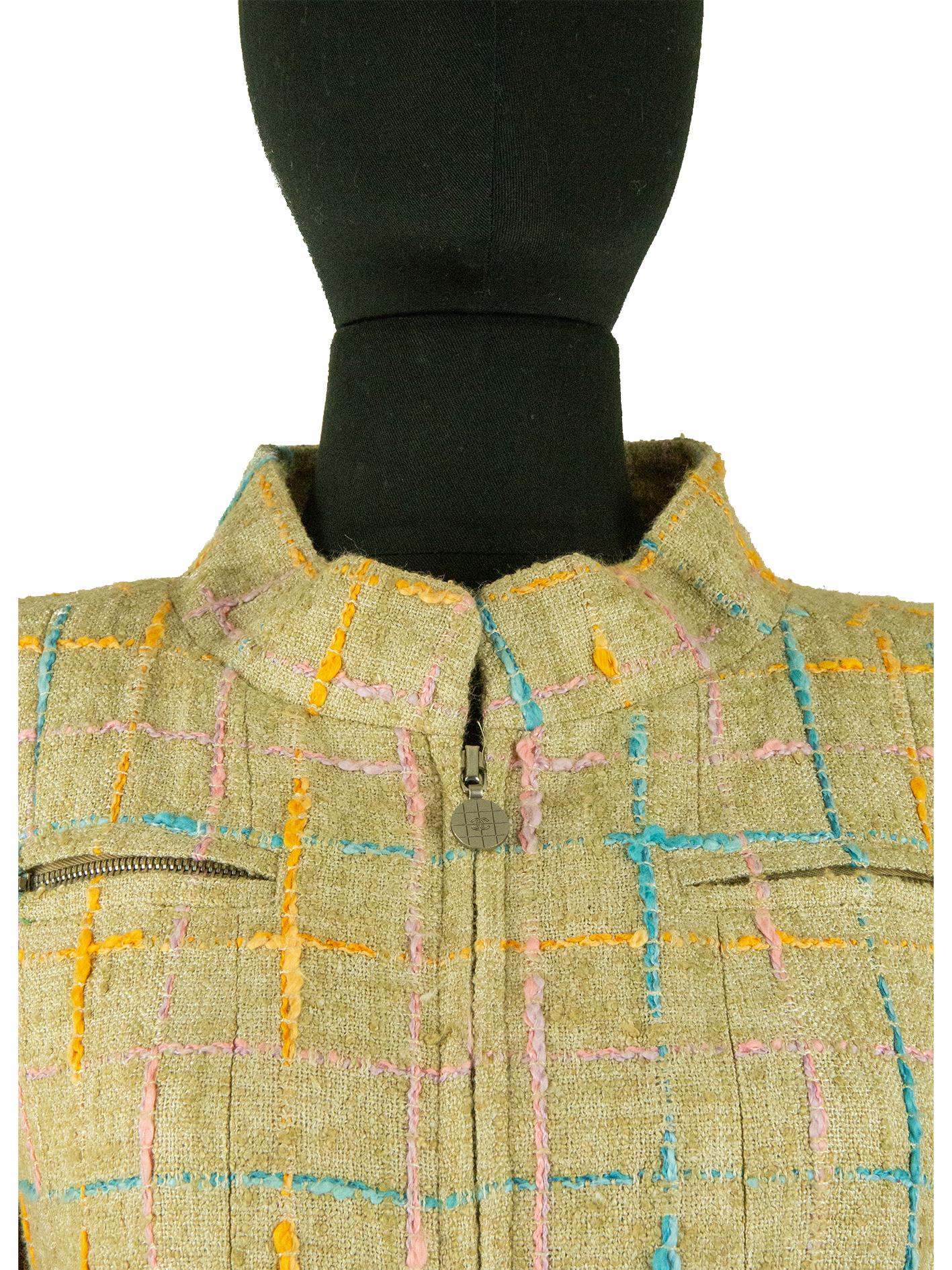 Un manteau beige Chanel du début du siècle avec des carreaux roses, bleus et orange. Ce manteau présente un col montant et deux poches zippées sur la poitrine, ainsi que deux poches passepoilées sur les hanches. Il est également taillé pour une