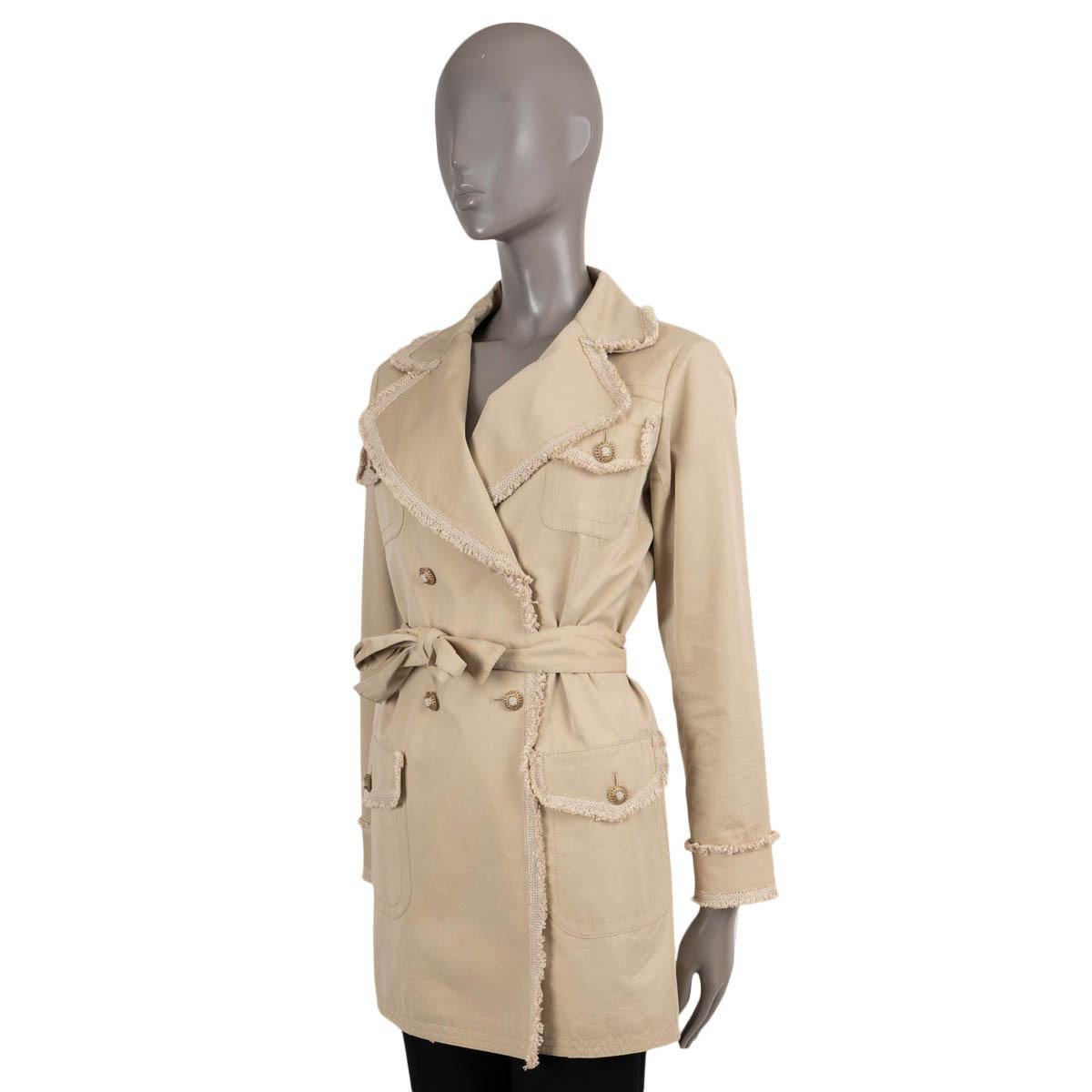 Trench-coat 100% authentique de Chanel en coton beige (70%) et soie (30%). Il présente des bordures en tweed effiloché, des revers en pointe et quatre poches à rabat boutonnées. Il se ferme à l'aide d'une double rangée de boutons et d'une ceinture