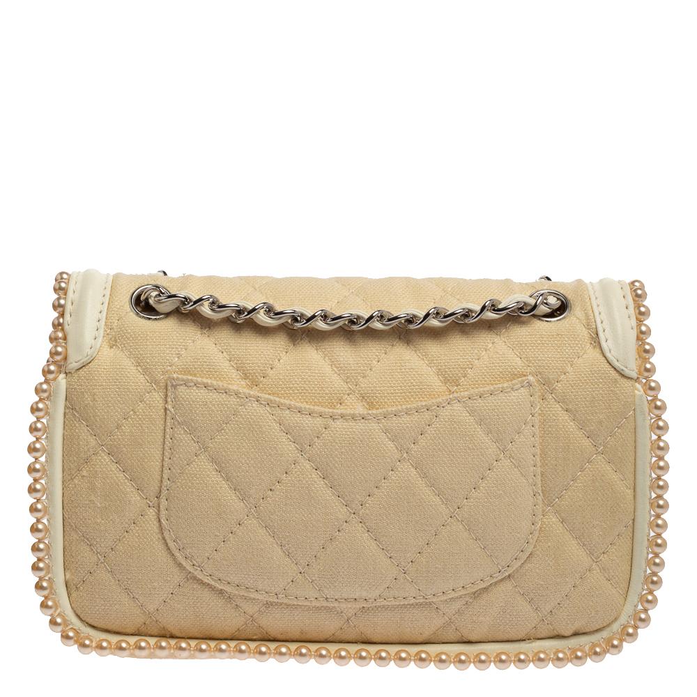 Diese Überschlagtasche von Chanel hat es uns angetan:: denn sie ist auf eine feminine Art und Weise ansprechend. Sie ist aus gestepptem Canvas und Leder gefertigt und mit hübschen Kunstperlenverzierungen an den Konturen versehen. Sie trägt das