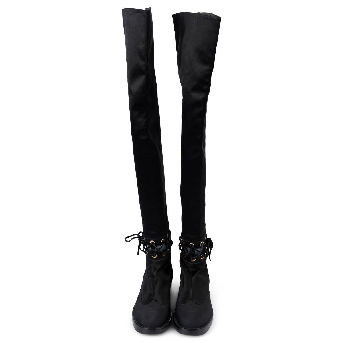 100% authentic Chanel interlocking cut-out over-knee boots in black satin and leather. The design features a cut-out with suede laces, grosgrain cap toe and trim, gold-tone hardware and a stacked block heel. Opens with a zipper on the back. Have