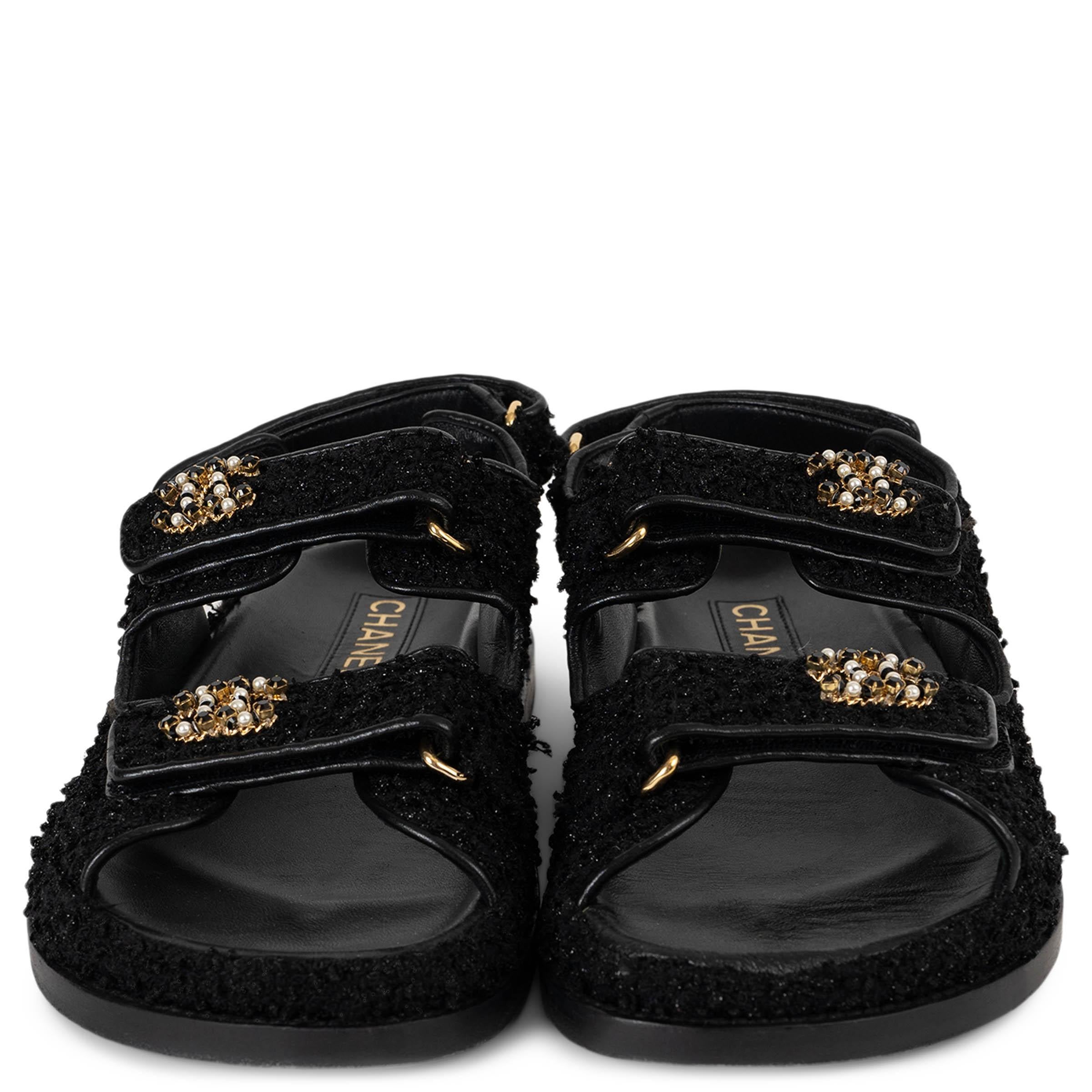 This 100% authentic Chanel Dad sandals in black glitter tweed bring a playful yet refined twist to the maison’s signature codes. Designed with rounded open toes, they feature two velcro straps across the front, each adorned with pearly white and