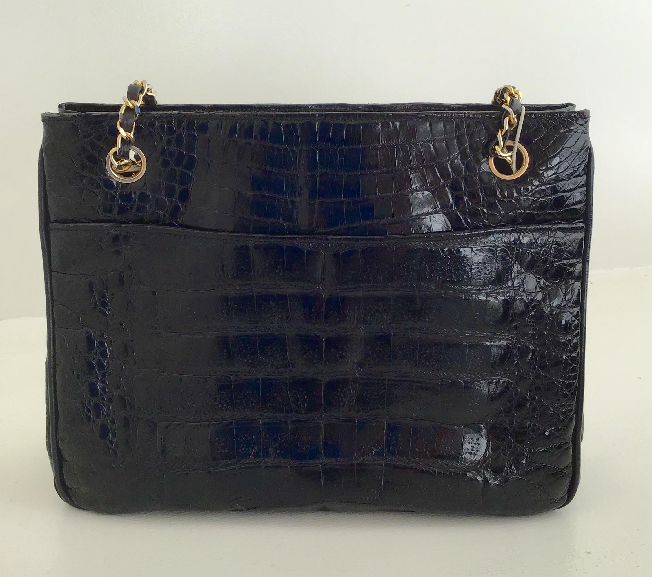Chanel Black Alligator Handbag. The leather-through-chain handle ends in a round piece of alligator leather adorned with a gold metal logo. The interior is lined in black leather and has two zipped pockets, while the front face has a slide pocket.