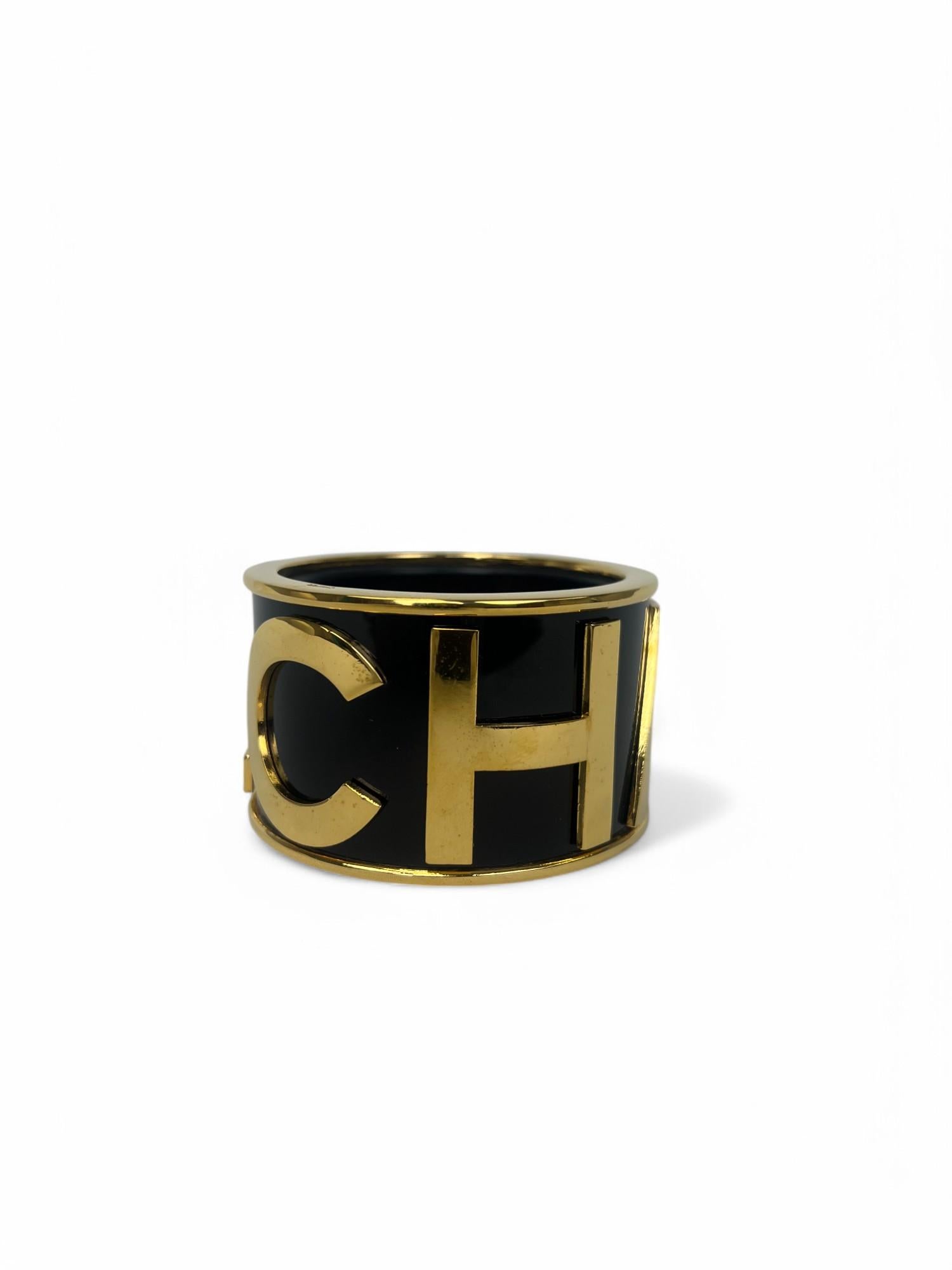 Striking and sculptural, this bold black and gold Chanel cuff is a powerful example of the house’s early '90s aesthetic under Karl Lagerfeld—where modern glamour met iconic branding with unapologetic flair.

Crafted in glossy black resin and