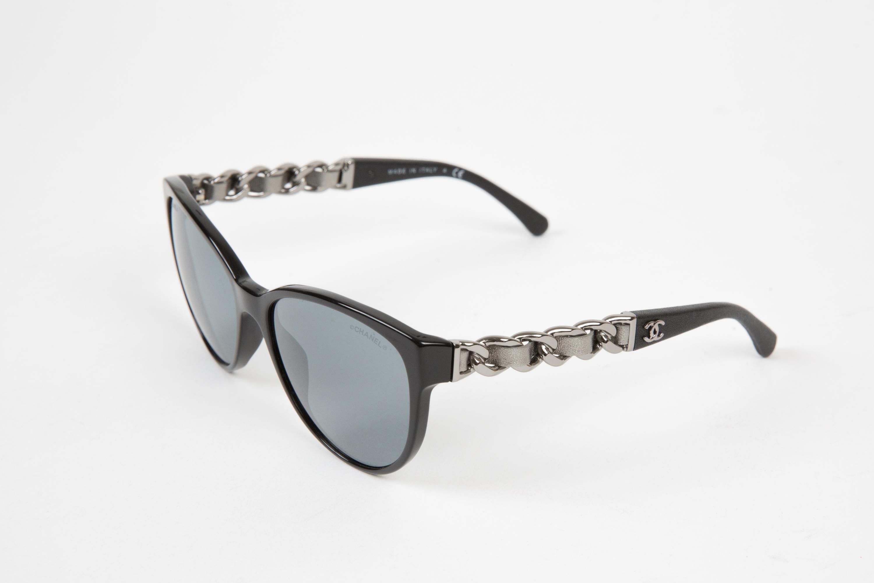 Chanel black cat-eye acetate sunglasses featuring silver-gold chain & Chanel signature detailing at the arm, cat-eye frame, straight arms with curved tips. 
100% acetate.Circa 2000s.  
Arm Length 5.5in. (14cm)
Lens length:2.1in. (5.6cm)
Total width: