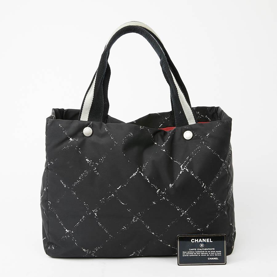 CHANEL tote in patterned canvas: black and white quilted, lined in red canvas with a zipped pocket on each side. The jewelry is silver metal.
It can be worn on the shoulder or elbow with its double handle in cotton canvas. Under the bag, there are