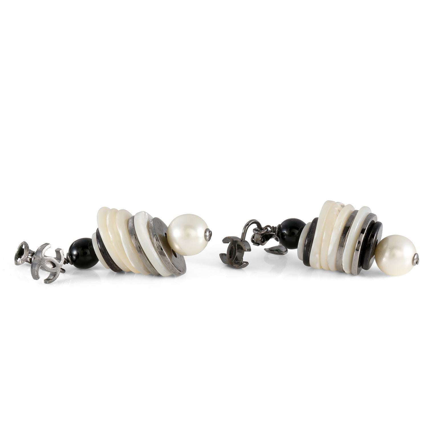 These authentic Chanel Black and White Layered Button Earrings are in excellent condition.  Silver metal interlocking cc on pierced lever back. Layered buttons are stacked between a black bead and a faux pearl. Pouch or box included.
