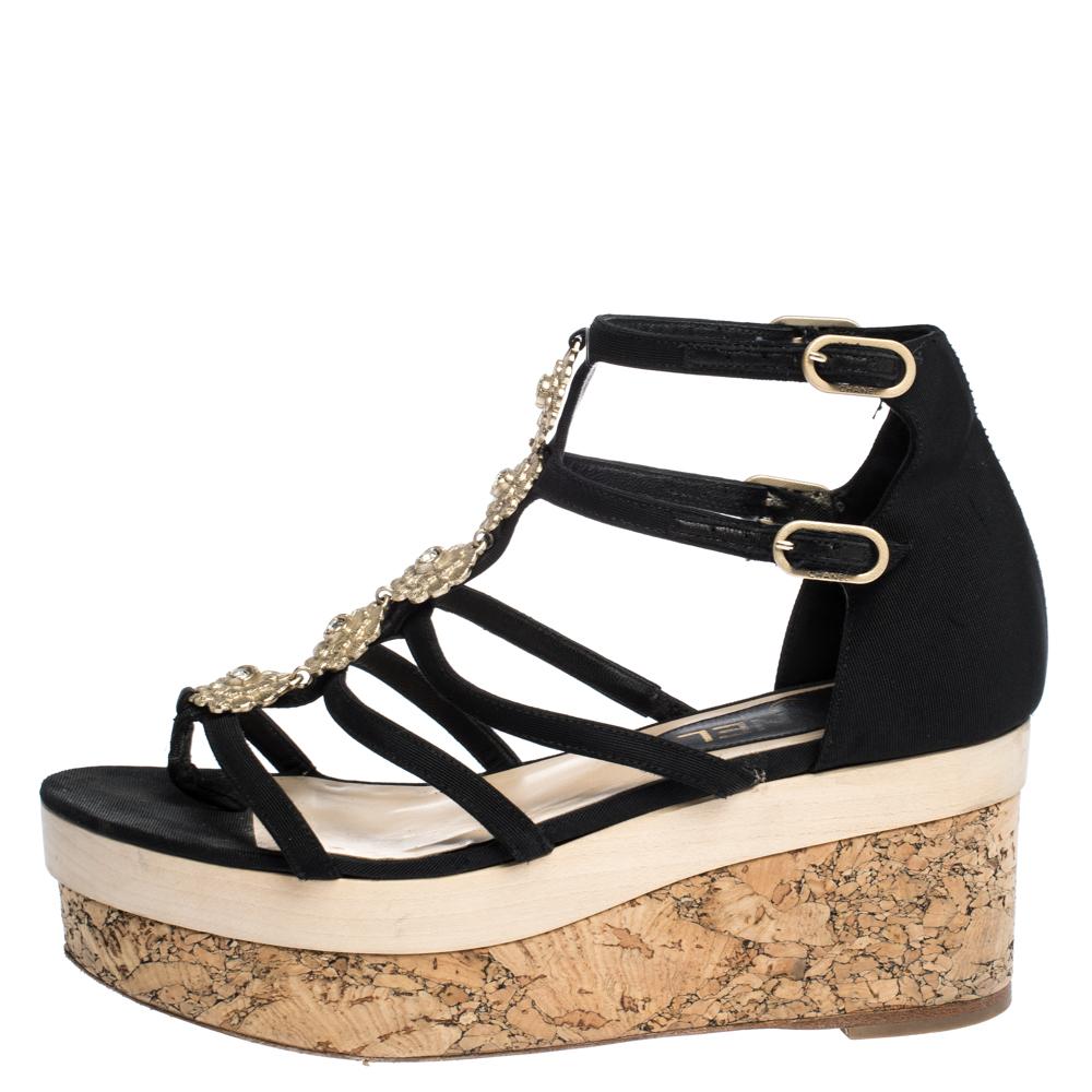 These Chanel sandals are loved for their right dose of vibrancy. Crafted from black canvas, they feature open toes, strappy vamps accented with floral embellishments, and gold-tone buckles on ankle straps. Elevated on cork platform, the insoles are